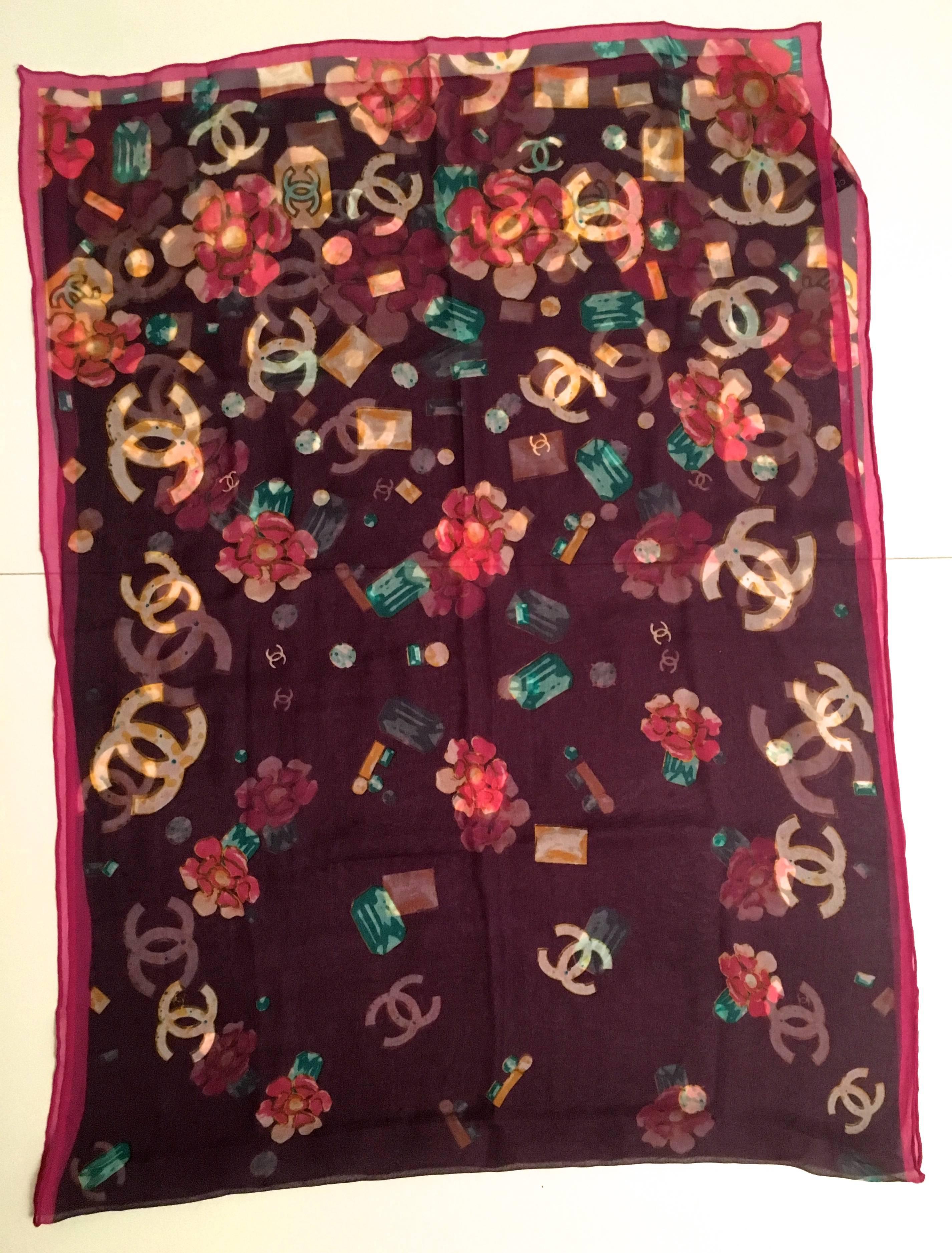 Presented here is a beautiful silk muslin scarf from Chanel. This magnificent scarf is comprised of a beautiful aubergine background with images of gem stones of varying colors throughout the design. The iconic CC logo is adorned throughout the