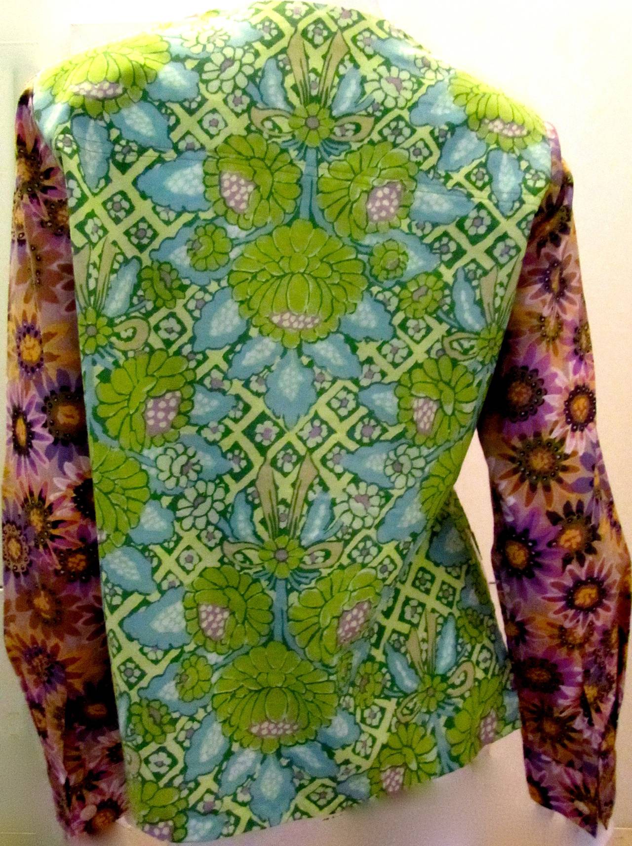 Koos Van Den Akker shirt from the 1970's. Gorgeous floral design print consisting of green, purple, yellow, and blue. The shirt has ruffles down the front of the shirt. The flower design on the exterior of the shirt is classic Koos at its very