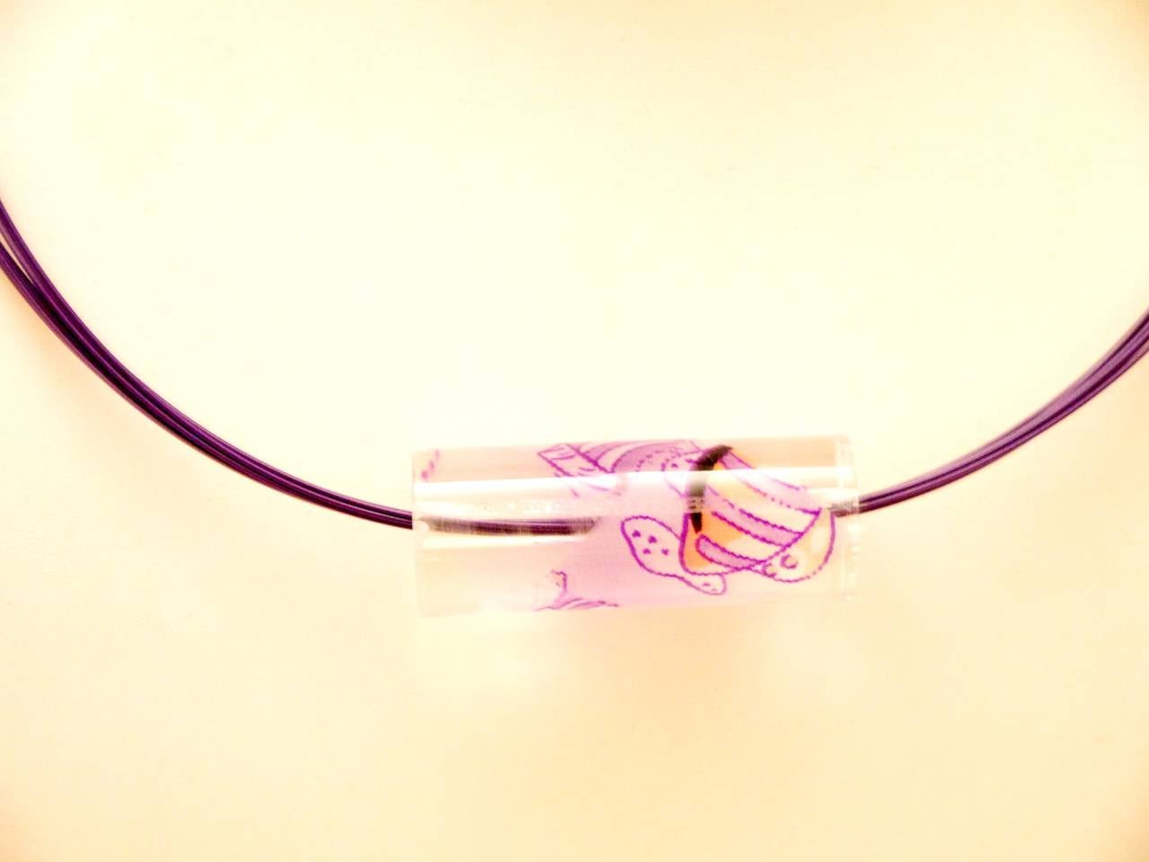 Extremely rare Hermes Purple and clear necklace. Necklace is a lucite cylinder adorned with fish graphics. The necklace strap is comprised of multiple thin plastic cords with a twist clasp enclosure. Total length of necklace strap is 17.6