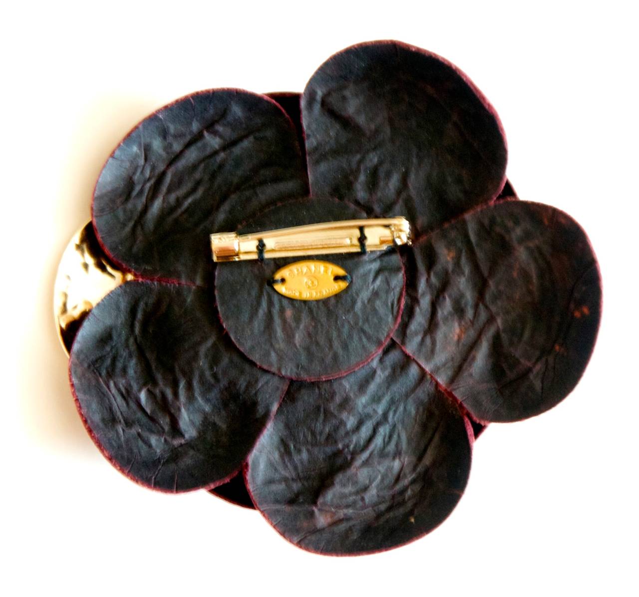 Chanel lambskin leather and brass camellia flower pin. Beautiful camellia in a rich burgundy lambskin. One of the pedals is a hammered brass with an embossed Chanel CC logo. Pin is also signed on back with small brass Chanel insignia. Truly a