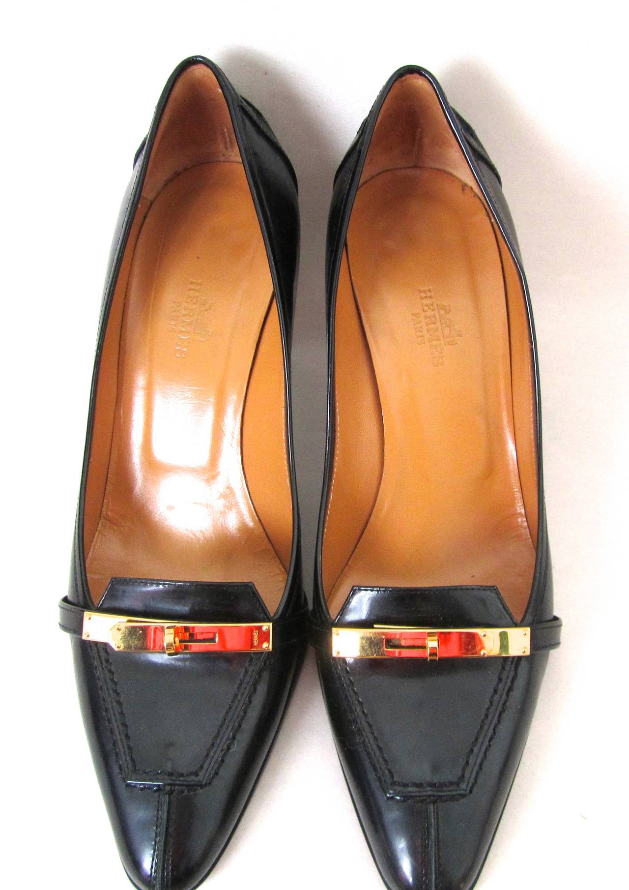 Hermes black leather pumps. The shoes are adorned with iconic gold tone kelly style hardware on the front of the shoes. Fantastic shoes with a classic look that is excellent for various occasions. Minor wear, but overall excellent condition.