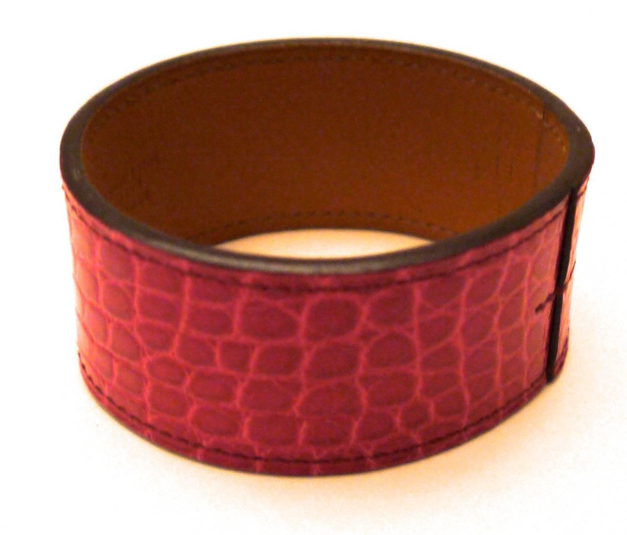 New Hermes alligator bracelet in fuchsia. This bracelet is a stunning addition to any ensemble and is a work of remarkable craftsmanship. The circumference of the inside of the bracelet is 8 inches. The diameter of the bracelet is 2.5 inches. The
