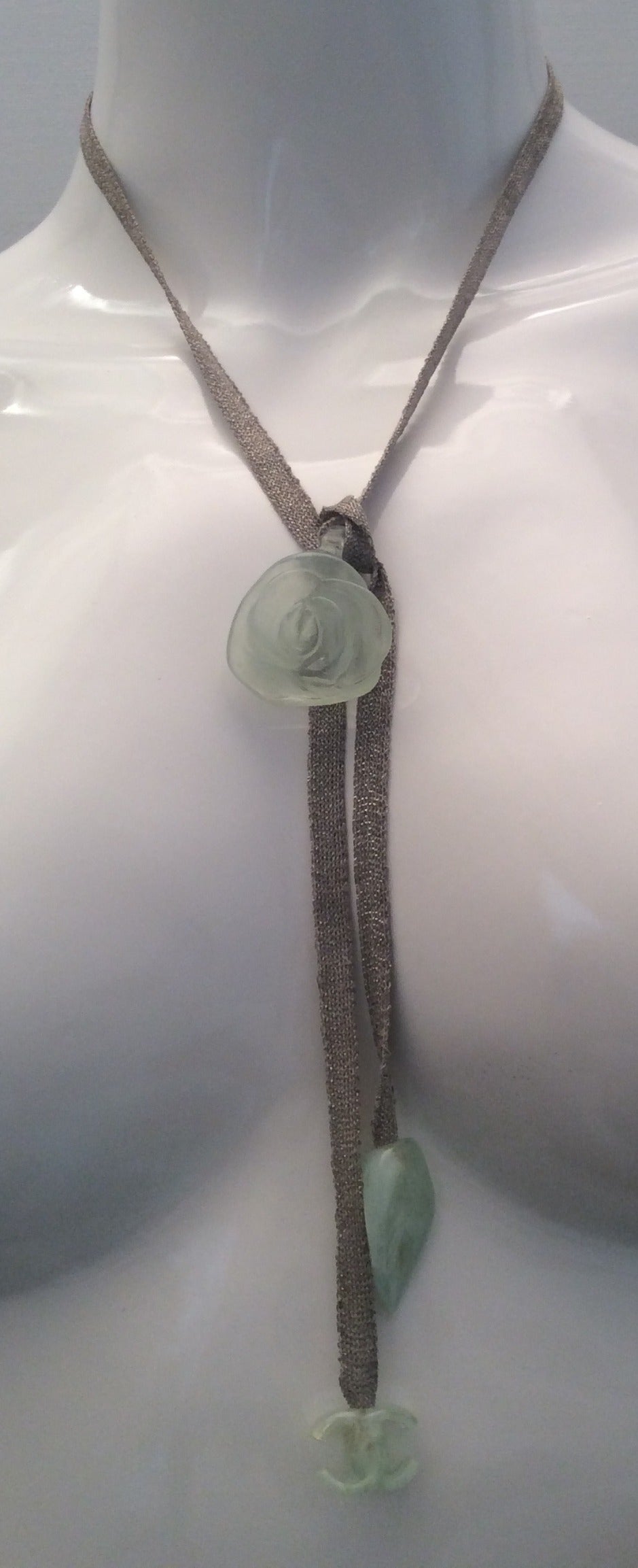 This beautiful Chanel necklace consists of a silver ribbon which starts with a beautiful leaf design in an opalescent creme tone with underlying detection of a greenish tone. It is signed at the bottom of the leaf. The other end of the necklace ends