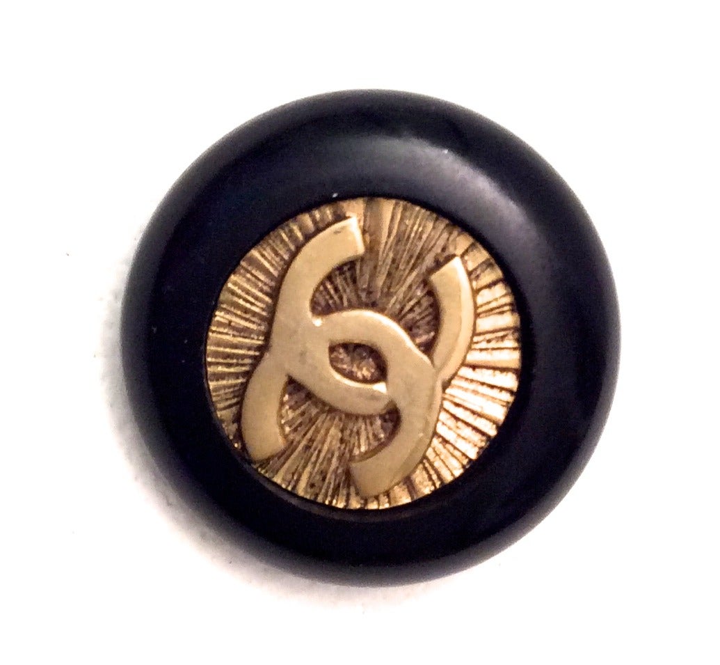 10 Vintage 1980's Chanel buttons. The buttons are black plastic with gold tone metal in the center of the button. The black plastic encases a gold tone embossed iconic CC logo with matte finish starburst design in the background of the button