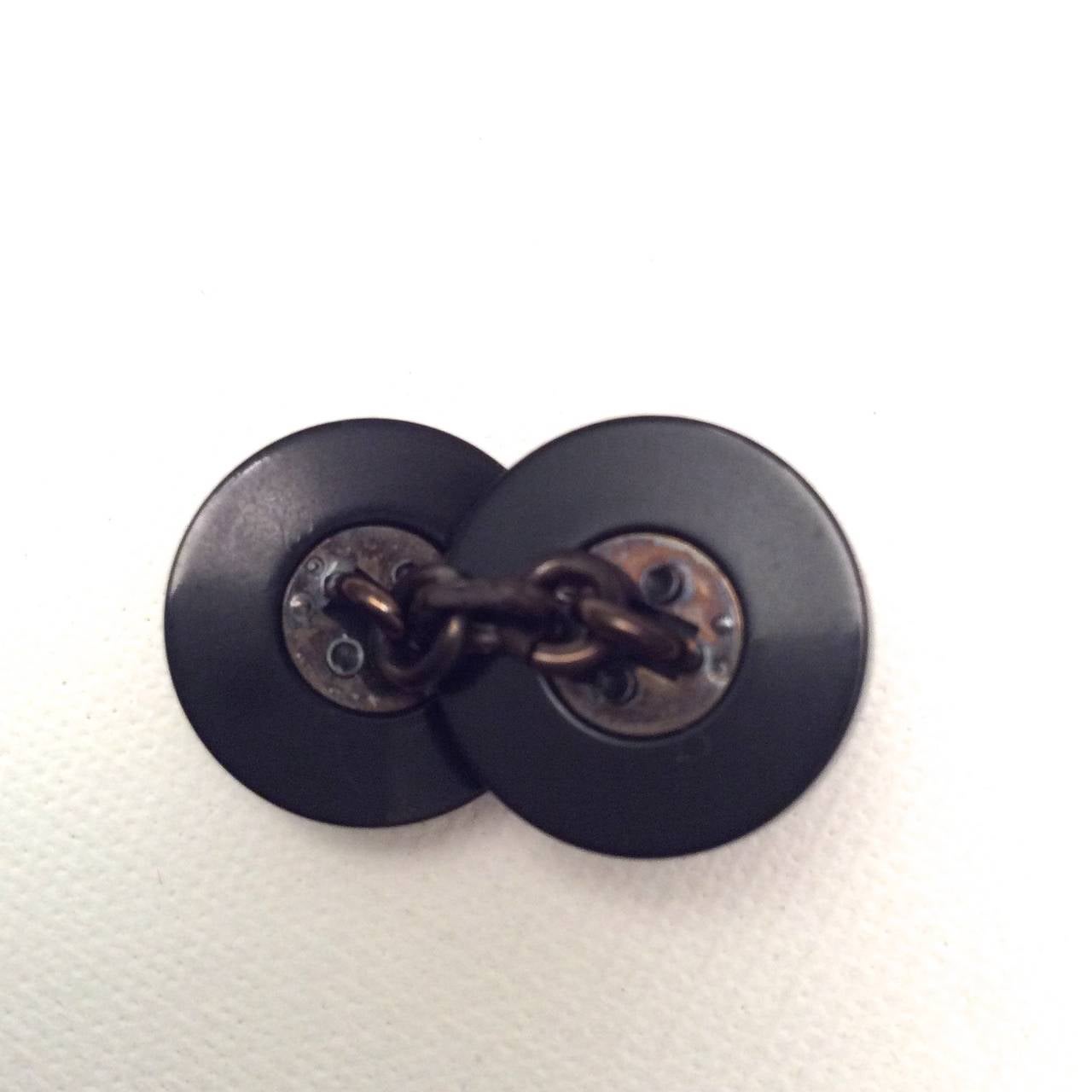 A pair of Chanel black cufflinks with CC logo. There is a Chanel signature on the inside of each of the buttons of the cufflinks. The exterior of each of the cufflink buttons has an embossed iconic Chanel CC logo. The cufflinks are from the 1980's.