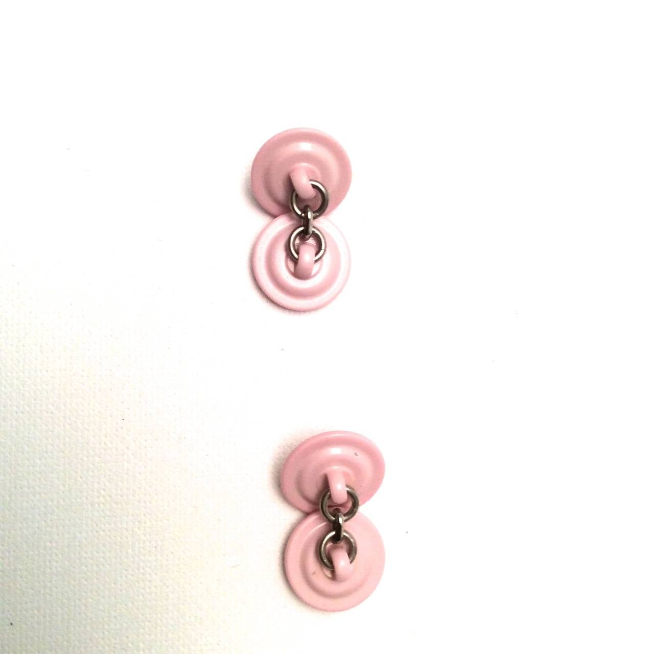 A pair of pink and white Chanel cufflinks from the 1980's. Each circular button on each end of the cufflinks is .6 inches. There is a chain that holds each half together. The cufflinks are a light pink with a cream white CC logo. A great addition to