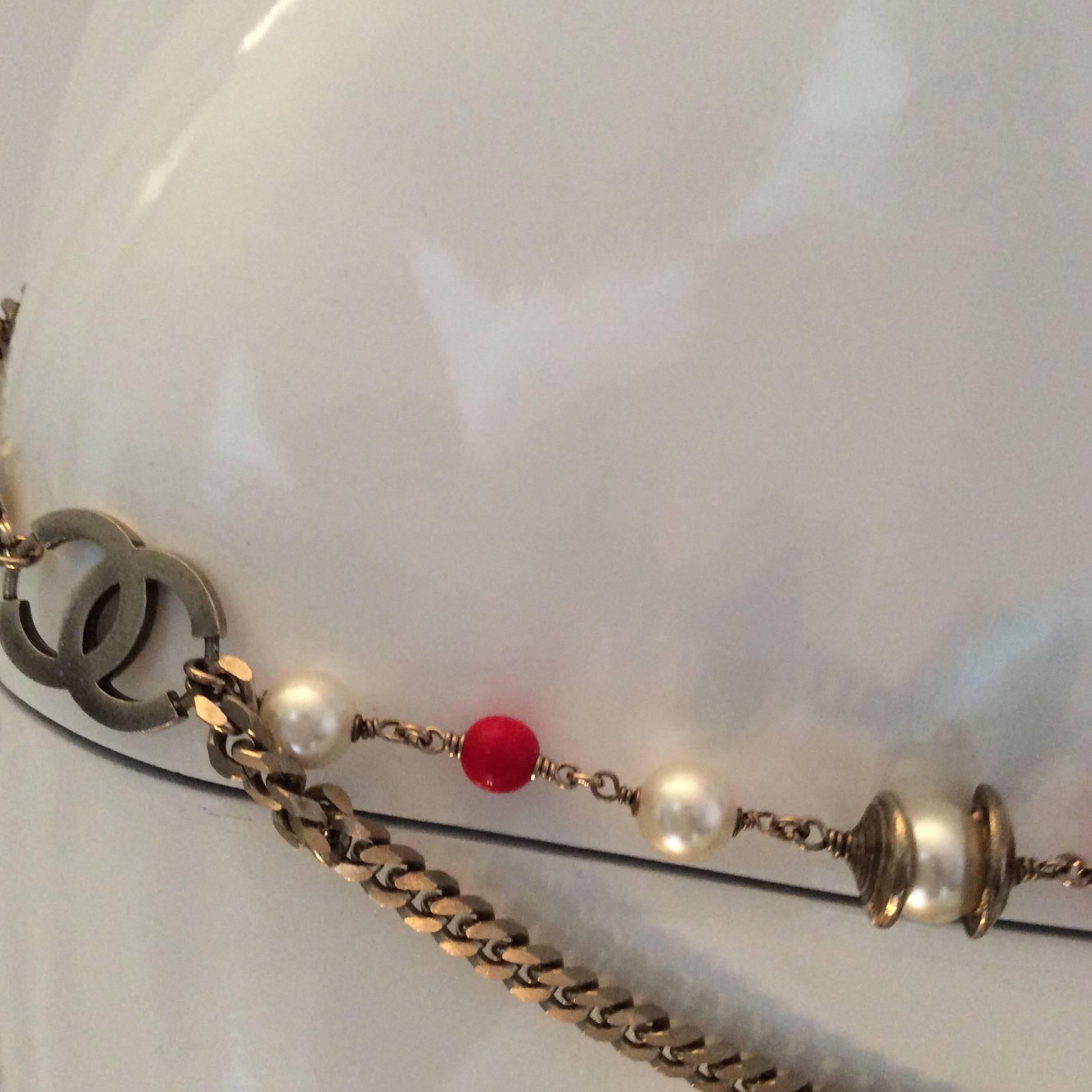 This is a silver tone Chanel belt which can also double as a necklace. I have never even seen one similar to it. It is signed '05 C. The belt / necklace comprises 2 CC emblems that are silver tone and are connected by a string of pearl and red