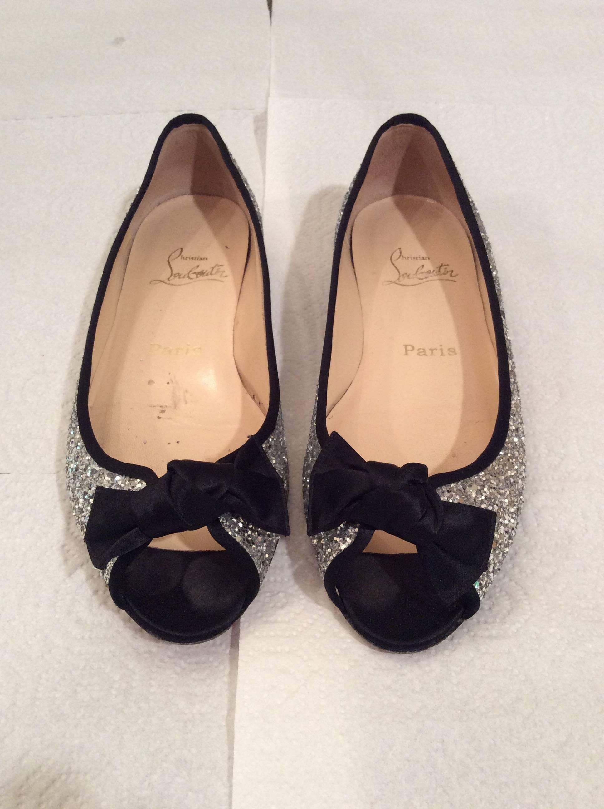 You are looking at a beautiful pair of gently worn Christian Louboutin size 37.5 open toed with silver sparkles trimmed in black silk bow in the front. Bottom of shoe has been replaced with a red anti-slip vibram sole. 

Length of shoe - 9.5