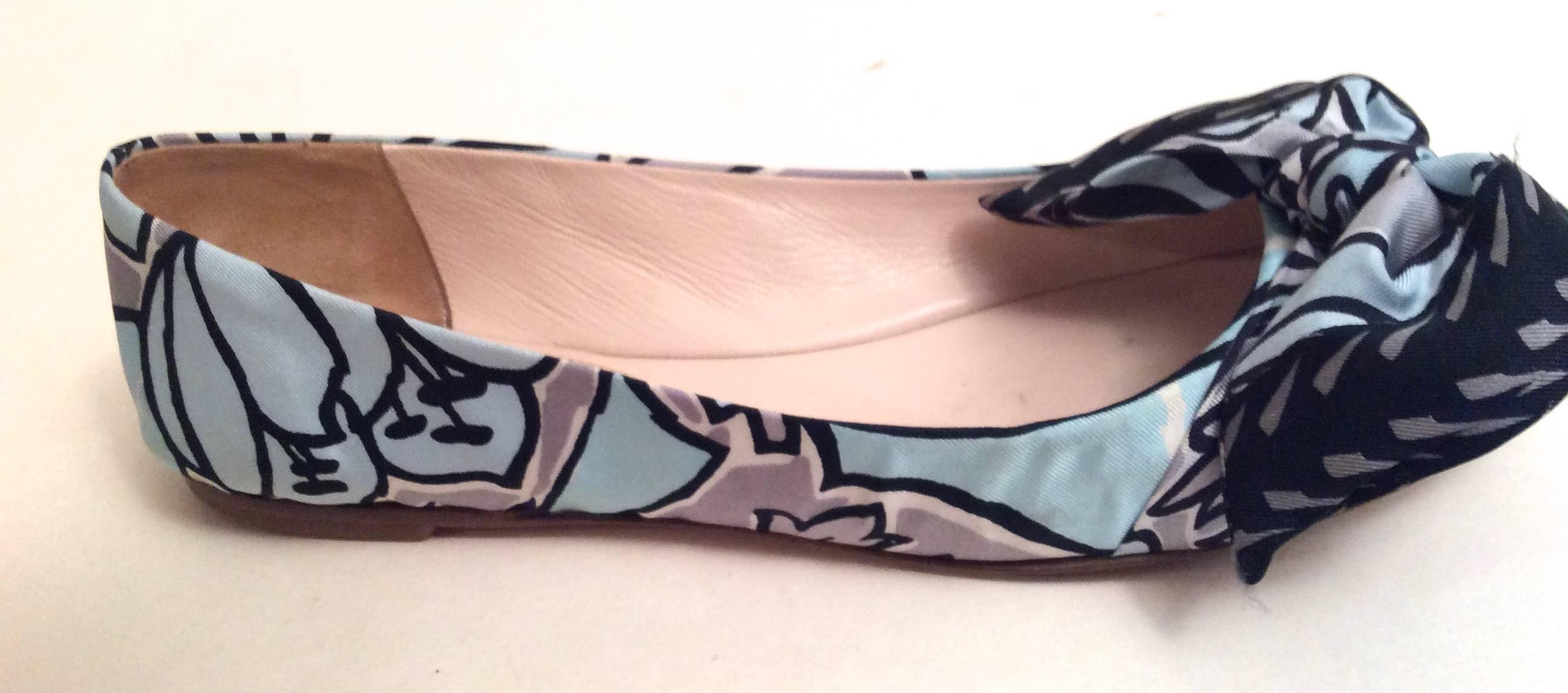 Here is a pair of size 39.5 Prada graphic flats. They are light blue with a geometric floral print along the exterior of the shoes with a bow at the toe of the shoes. They are a versatile flat that makes for a great shoe for various occasions. They