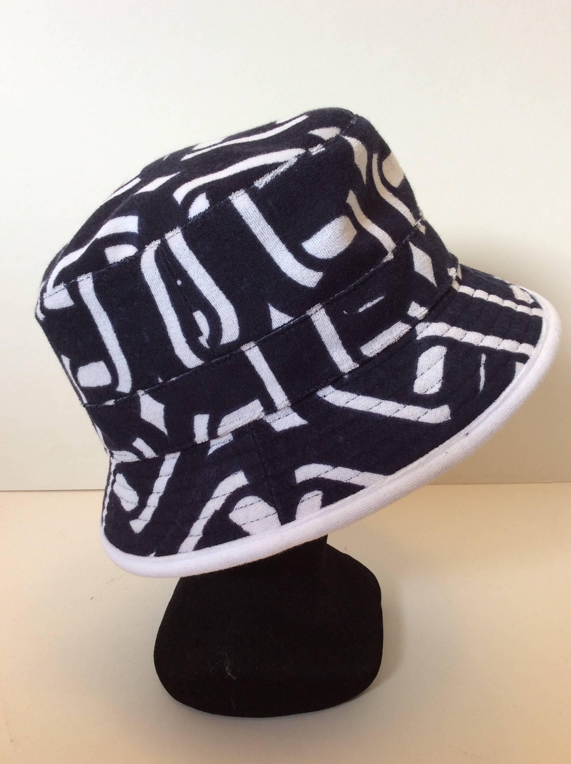 This Hermes terry cloth hat is available in size 58. It is a versatile hat for varying occasions and makes a subtle but significant statement. It is dark navy blue and white and has a unique Hermes print throughout the exterior of the hat. It is a