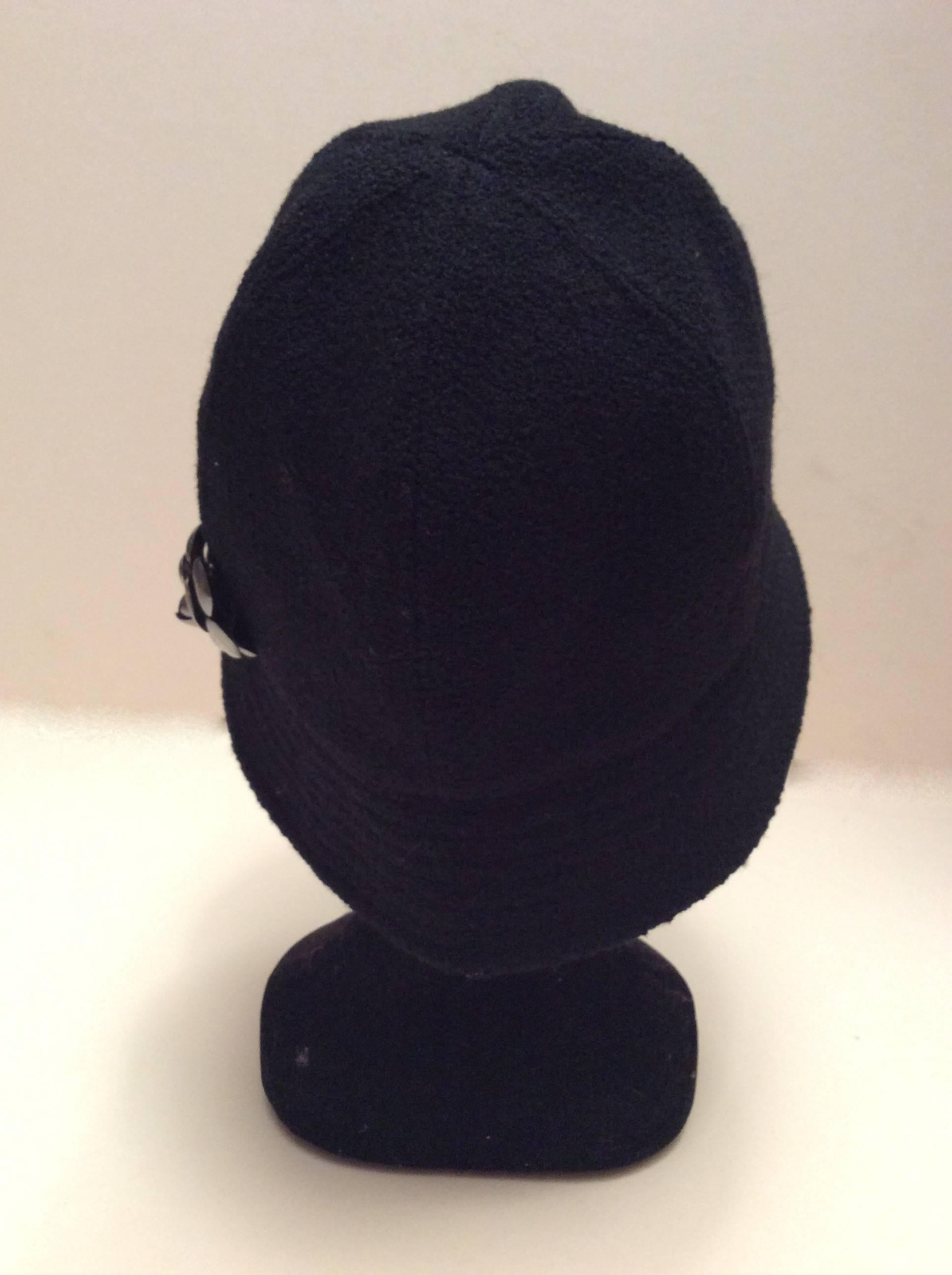 Here is a magnificent Chanel hat that is made of black boucle fabric. It is size 57 is adorned with a gray silver tone metal camellia emblem on the exterior of the hat. There is a 2.1 inche rim around the exterior of the hat. There is 8.5 inches of