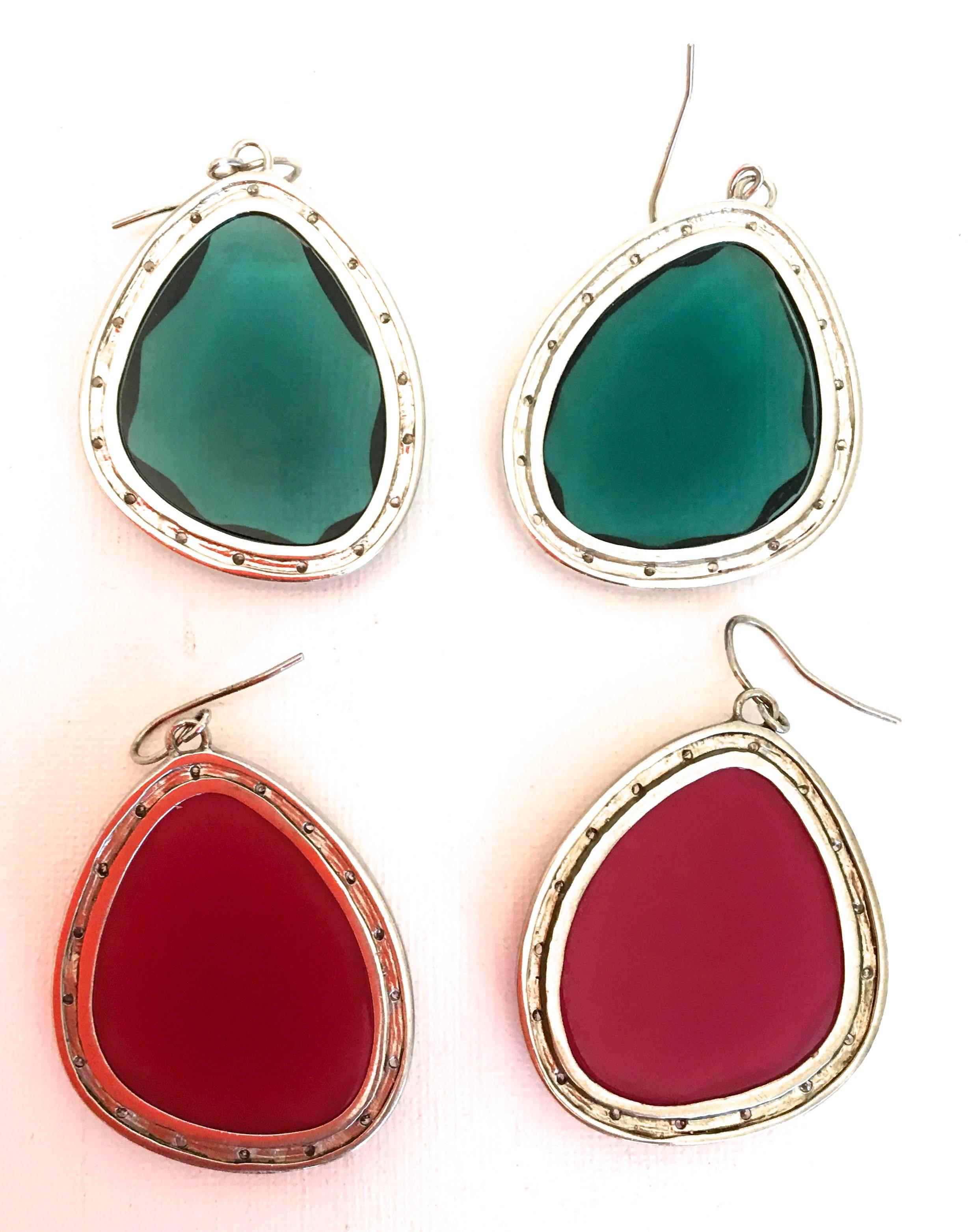 Presented here are two pairs of earrings from Miriam Salat. The earrings are comprised of a sterling silver frame and hook. Inside the frame there is a large colored stone. Around the exterior of the front of each earring there are small cubic