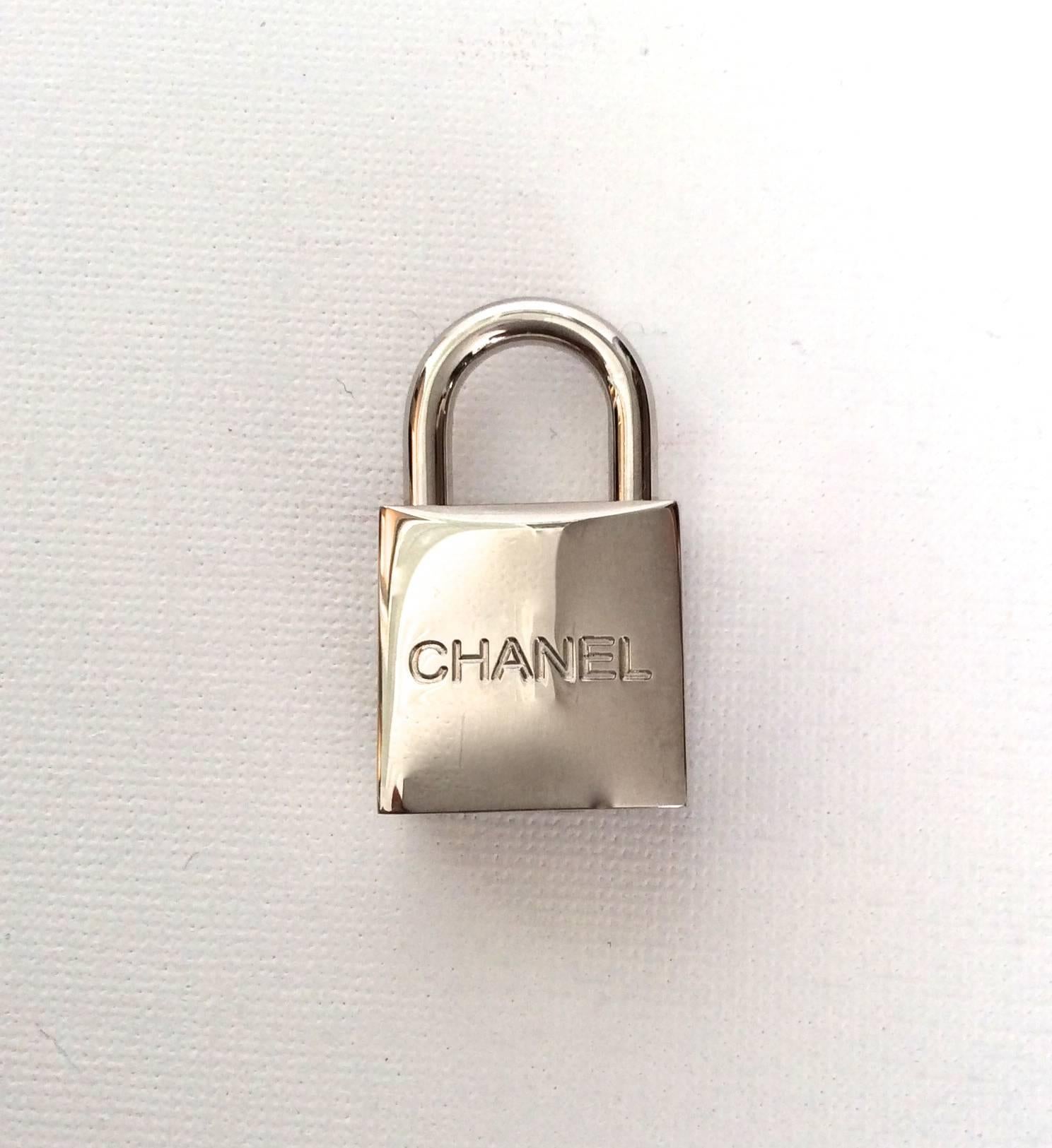 Chanel luggage lock for handbag and luggage. The lock is silver palladium metal and locks and opens with a key. The lock is 1.4 inches tall and .75 inches wide. There is an embossed 'CC' logo on the back of the lock and the front of the lock there
