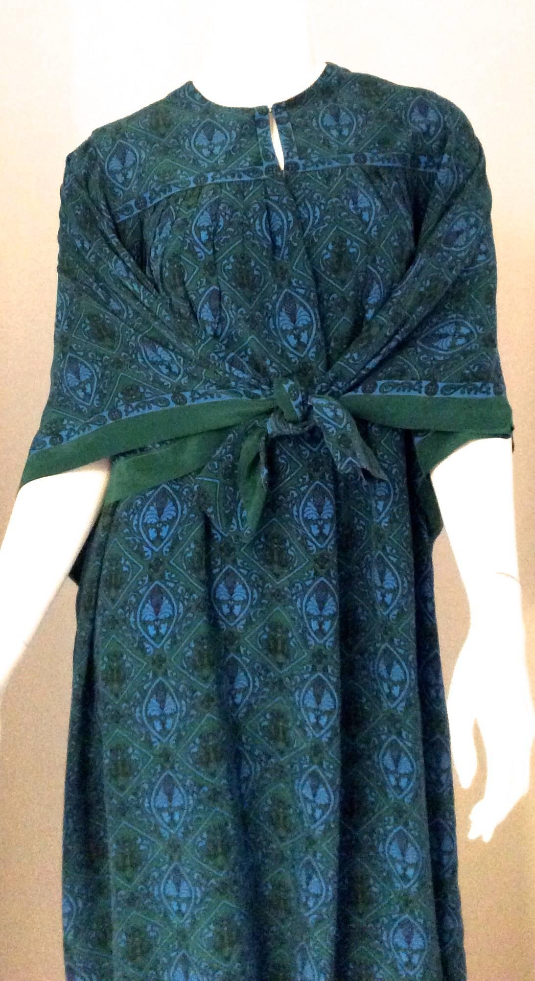Presented here is a magnificent Serge Lepage Schiaparelli Caftan dress. The dress is an emerald green background with a turquoise blue geometric design.  The front of the dress has an opening of 8 inches with two snap closures. The dress is not