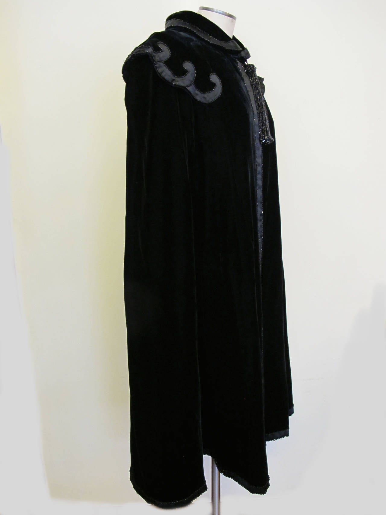 Iconic, luxurious Yves St. Laurent Rive Gauche Black Velvet Cape with scallop bugle beads and 7.5 inch Black Bugle Bead Tassel. Fits small to large due to
design of cape. Two black satin 3/4 inch panels with bugle beads adorn the front of the cape.