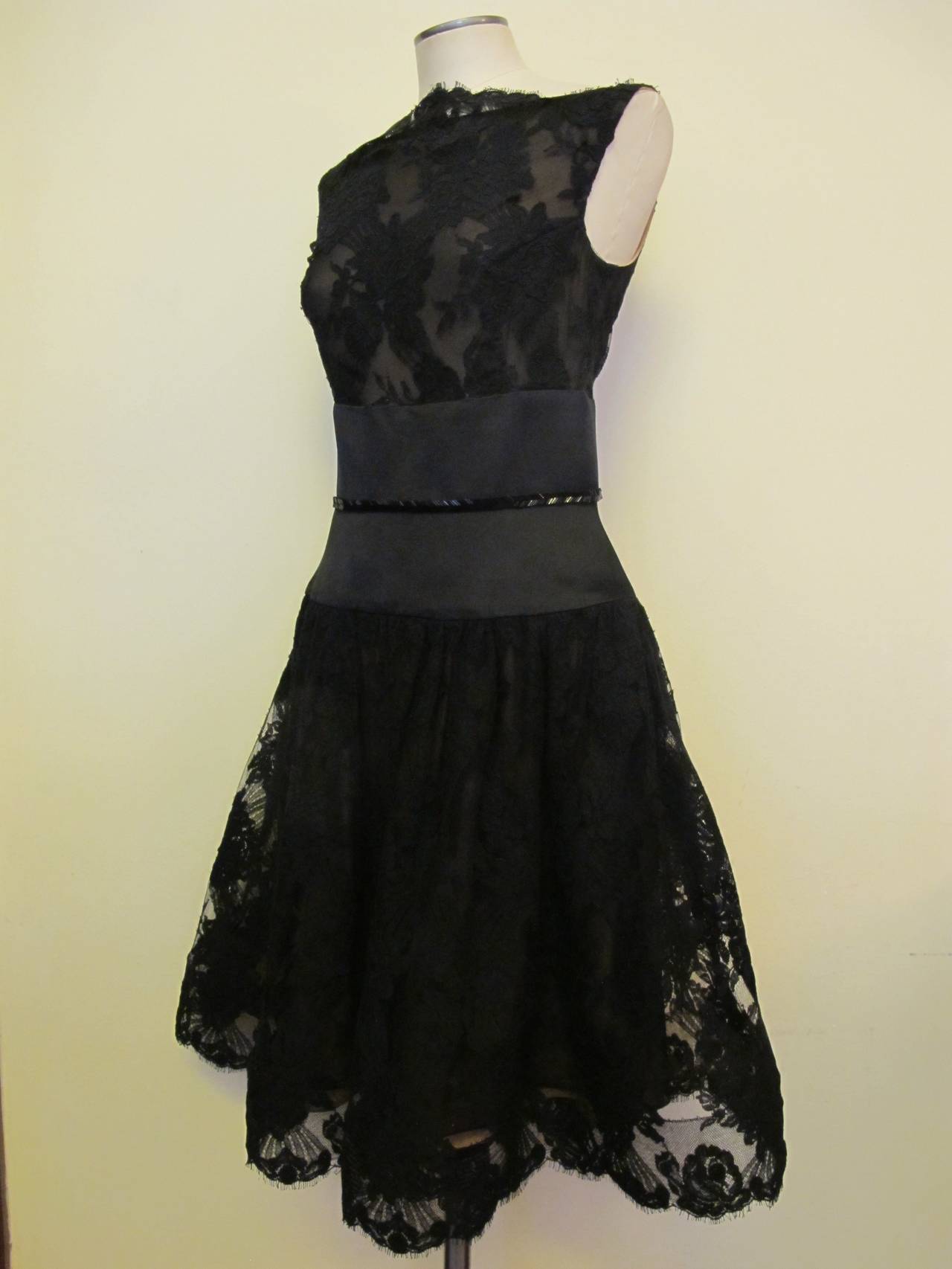 This exquisite black bateau neckline cocktail dress has an empire waist of duchess black satin and strip of black bugle beads in a chevron design. Alençon lace adorns the bodice and skirt of the cocktail dress and 2.75 inch horsehair gives body to