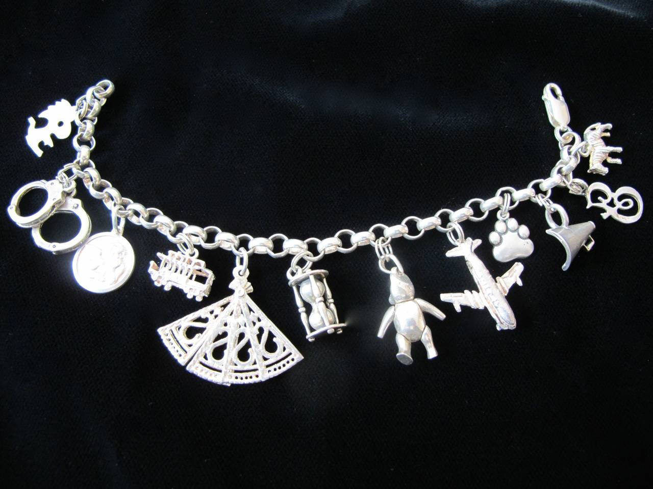 Engaging bracelet with twelve charms: Snoopy's Woodstock, pair of handcuffs, an angel, a cable car, a fan that opens, an hourglass, a teddy bear with moveable arms and legs, an airplane that opens, a paw print, a bull horn, the letter 