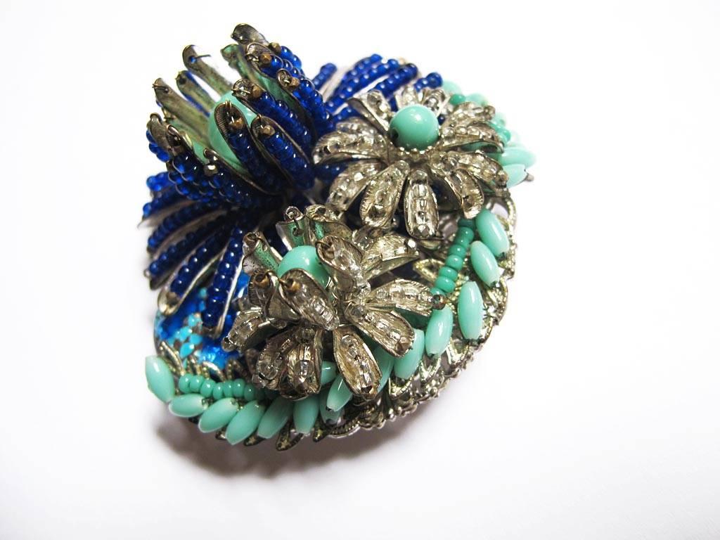 This 1950's vintage Miriam Haskell floral brooch is a masterpiece of hand sewn royal blue and turquoise pate de verre round and rice beads. The piece has multi layers of flowers and leaves making it three dimensional and all beads are wired in place
