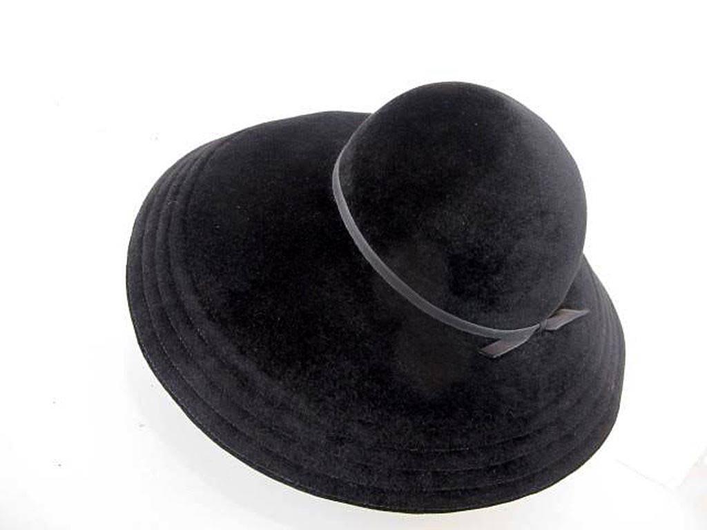 Black thick velour felt hat with wide brim. Trimmed with thin black grosgrain ribbon tied at back. Four rows of stitching decorate the brim of the hat with all the detail and quality James Galanos is known for.

Diameter: 7