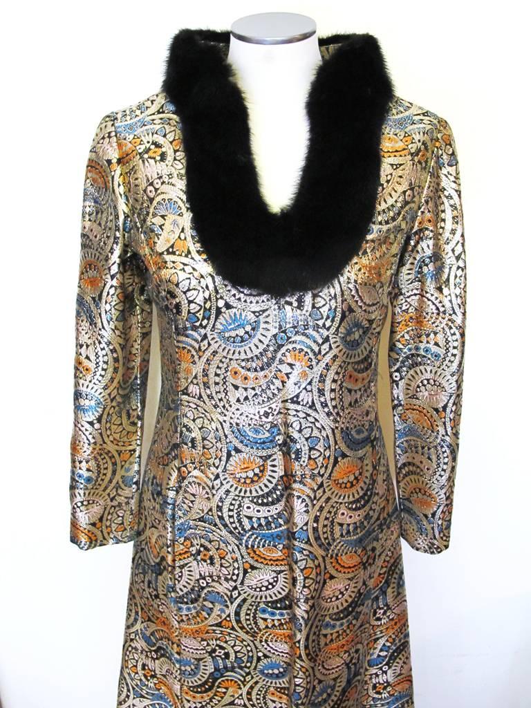 This impressive 1970's Malcolm Starr evening gown designed by Rizkallah has a black mink trimmed neckline. The beautiful gold metallic brocade fabric is in a paisley like print with orange, blue, and pink accents. There are two hidden pockets in the