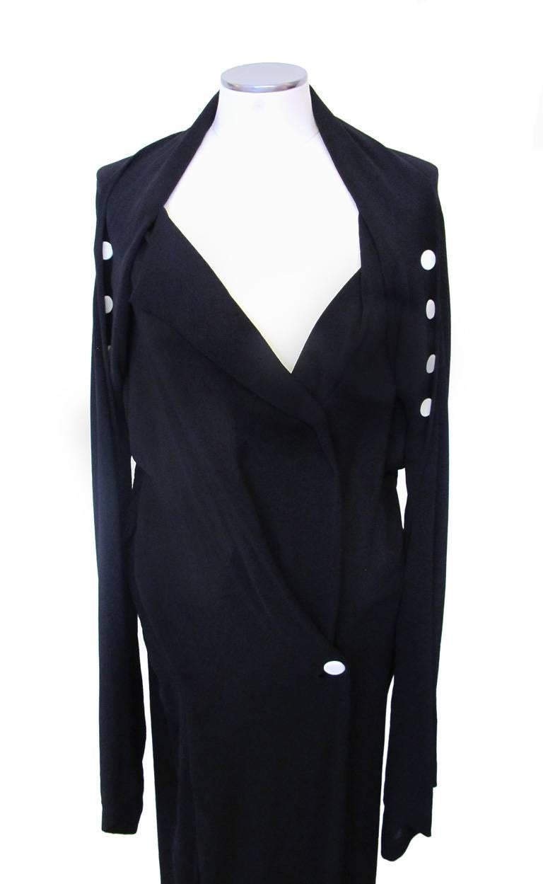 This chic Yohji Yamamoto black dress with white buttons has an asymmetrical neckline. The cut of the sleeves twist so that the buttons swirl down the arms. The sleeves end in a point. On the back side of the dress, the same white buttons accentuate