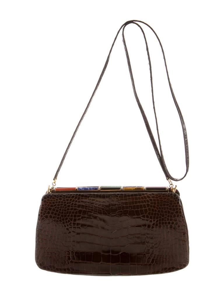 Chocolate alligator Judith Leiber shoulder bag with gold-tone hardware, flat shoulders strap, stone accents at top frame, chocolate satin lining, three compartments, single pocket at interior wall and kiss-lock closure at top.

It has a removable