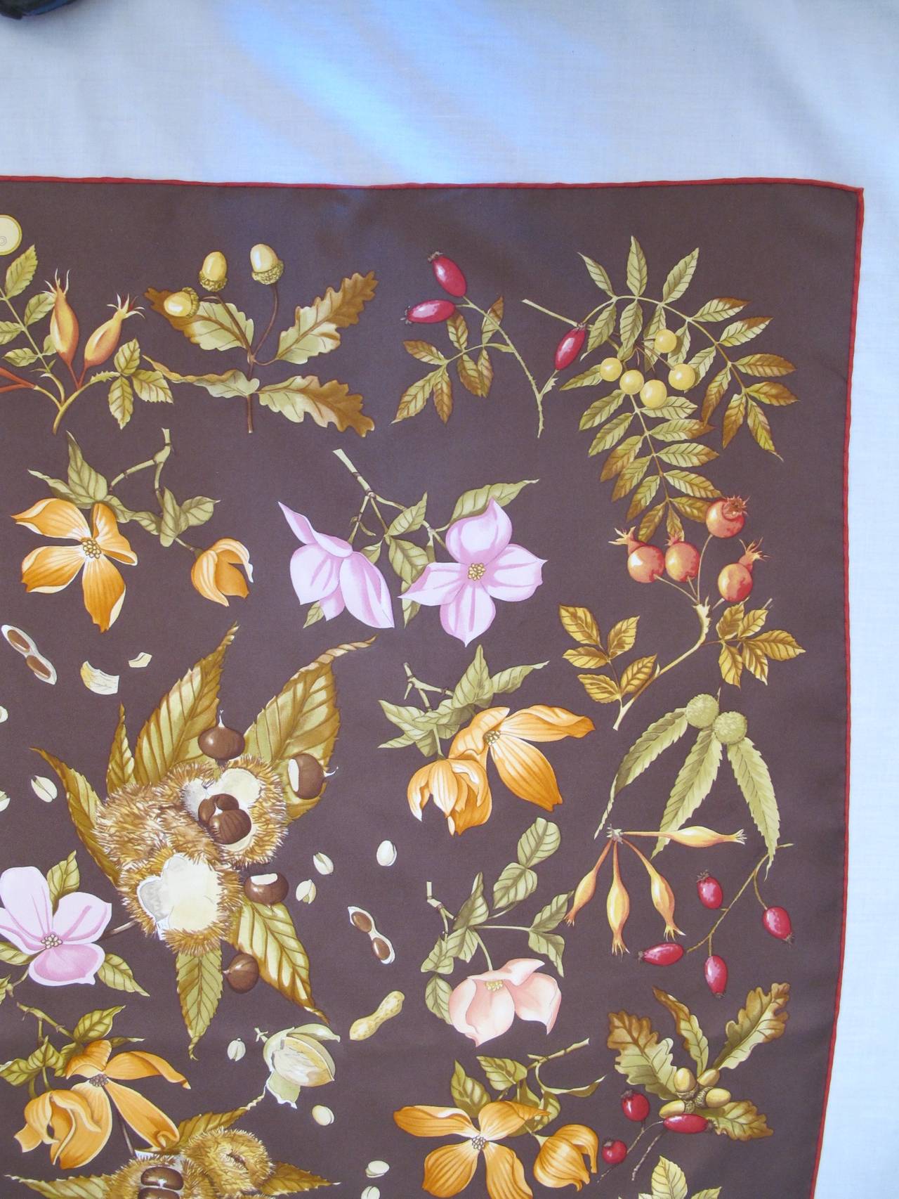 This scarf celebrates Autumn with the feeling of spring and blossoms. The background is a mixture of taupe and sable. Acorns are scattered throughout the scarf. The maroon border is hand rolled.