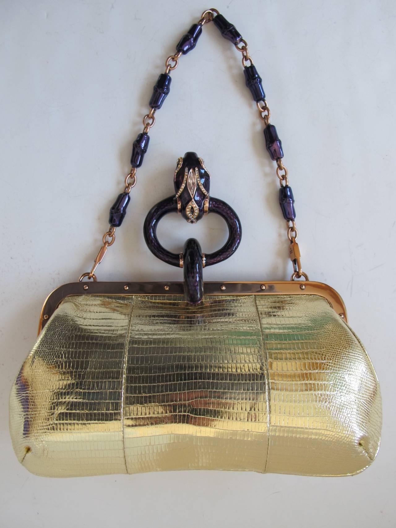 Tom Ford designed for Gucci this gold faux lizard leather purse. It has a purple cloisonné enamel clasp featuring a snake's head. The snake has a diamante on it and its mouth is clutching a round swarovski crystal ball. The chain handle is