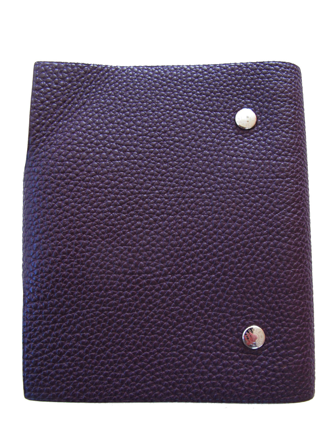 The Hermes Ulysse Eggplant Notebook has a leather tab with silver and palladium snap closure. Togo calfskin. The page refill notebook has the H plastic logo on the 1st page. The notebook itself has colorful pages: fuchsia, orange, light split pea