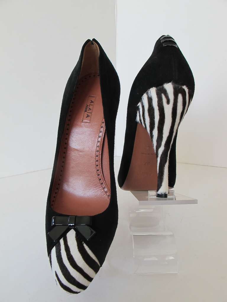 Stunning black suede Alaia pumps with toe and heel accented by zebra design. Zebra detail is stenciled calf with a small black patent leather bow in front and 3 black patent leather laces in back of shoe attached to black suede. Dust bags, original