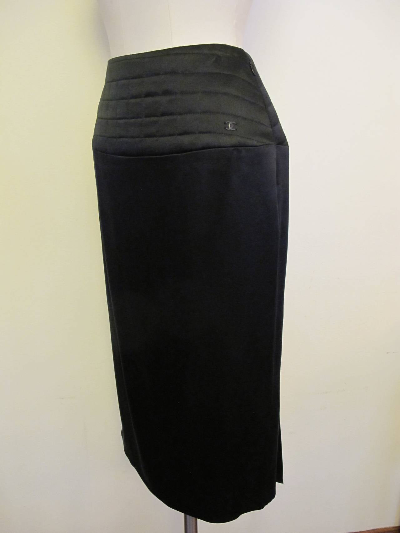 Elegant Chanel skirt with back pleating. An iconic black quilted design surrounds the 5 inch band across the waist. The pleated panel in the back covers the slit in the skirt. Chanel Logo appears on the waistband of skirt. Made in 2002.