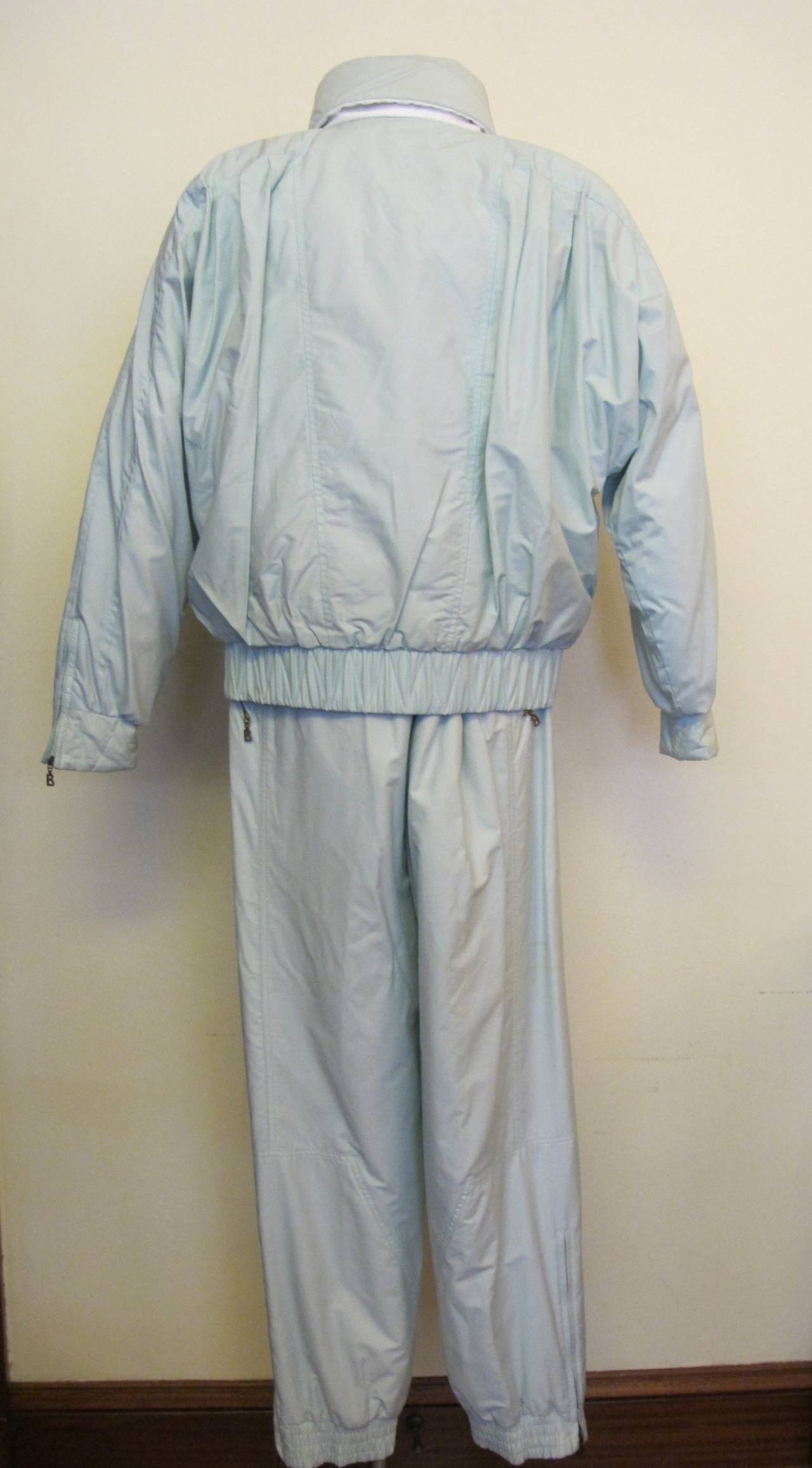 This ski suit is goose down filled. The sky blue color of this ski suit is heavenly. The jacket has a continuous sleeve with 2 zippered pockets with a zipper in front of the overlap and 2 zippers - one on each sleeve. It was donated to Helpers by a