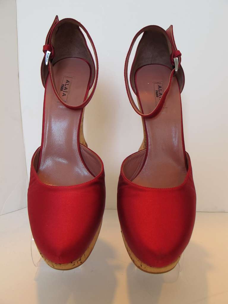 Fabulous red satin wedges designed by the master, Alaia. The color of the satin is divine. Ankle strap contributes to the chicness of the shoe. The red satin shoe, is created atop the chic cork.