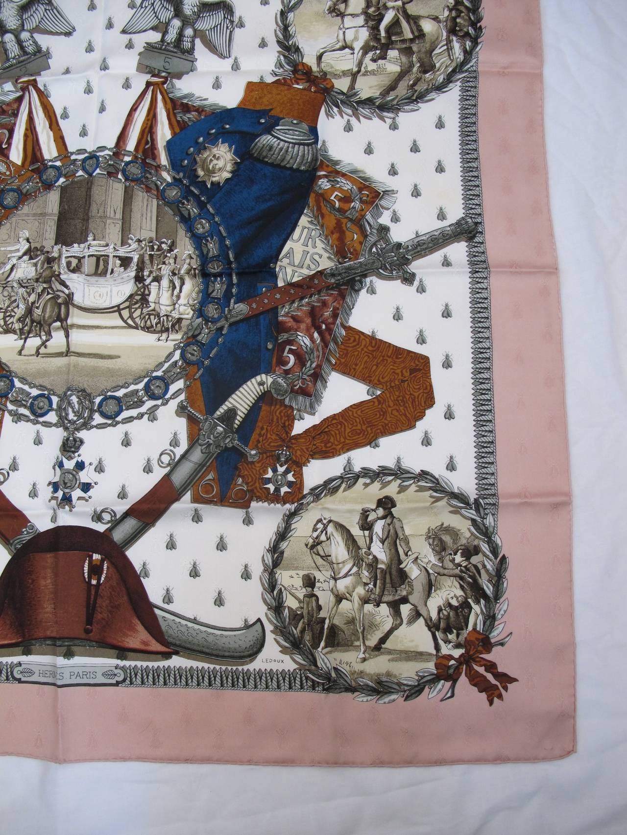 This elegant Napoleon silk scarf has a cream background with dusty pink borders. Images are in different shades of beige, brown, blue and gray. The images featured are: carriage drawn by horses, Napoleon on a horse and other French gentleman with