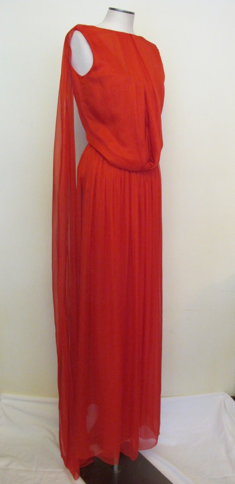 This exquisite red silk chiffon sleeveless evening gown is ready for the red carpet. The blouson bodice will accommodate a 34 or larger bust. There are two panels that gather in the front. Two panels are flying in back of gown, cascading from the