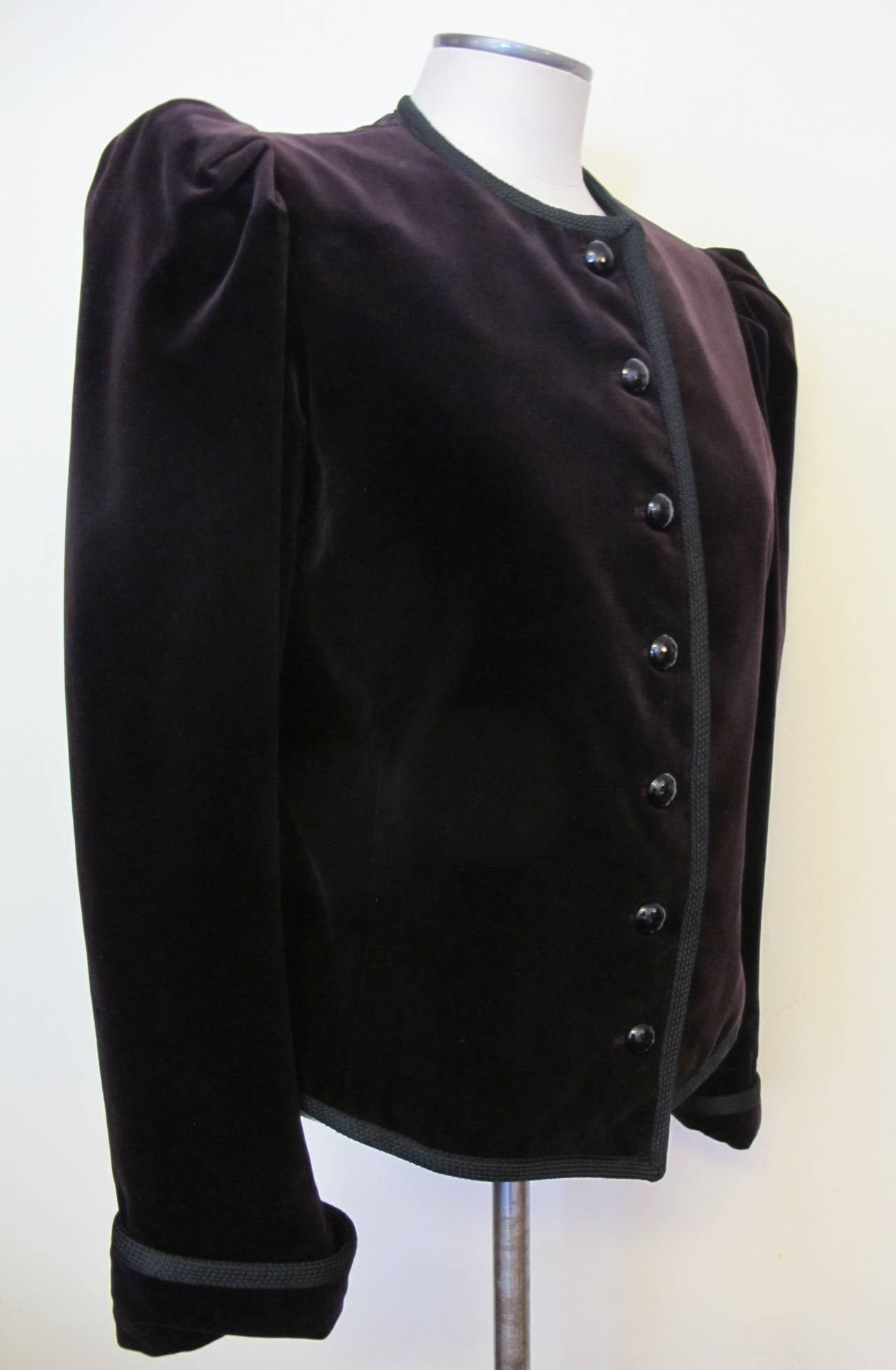 This iconic, rare aubergine velvet Yves St. Laurent jacket has seven onyx buttons and 1/4 inch braiding across collar, in center and on sleeves.

Shoulder to shoulder measures 14 inches.
Sleeve length measures 25 inches.