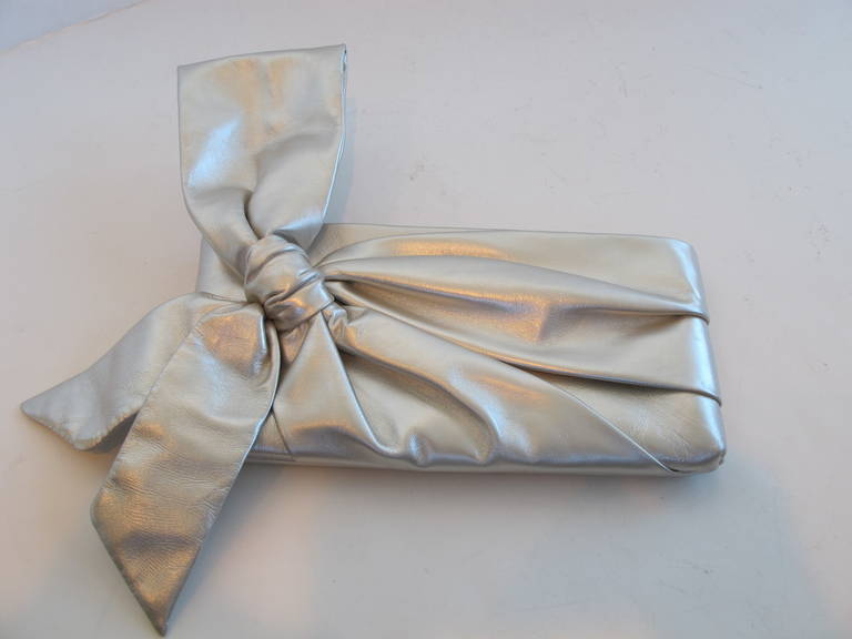 Iconic knotted bow Valentino Clutch which is accented by the rich pearl-silver color. The Italian made silver leather bow clutch has a gathered front that culminates in a statement bow.
