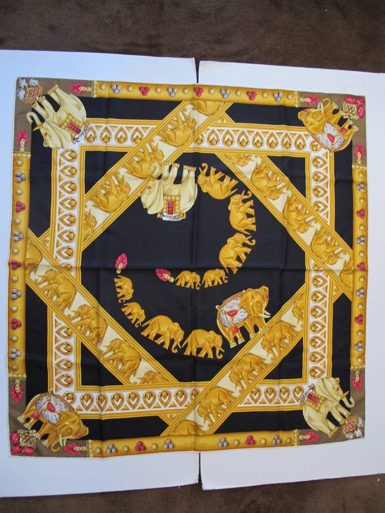 Iconic Cartier Scarf surrounded by elephants and Cartier jewelry. Features rich colors of gold and black.