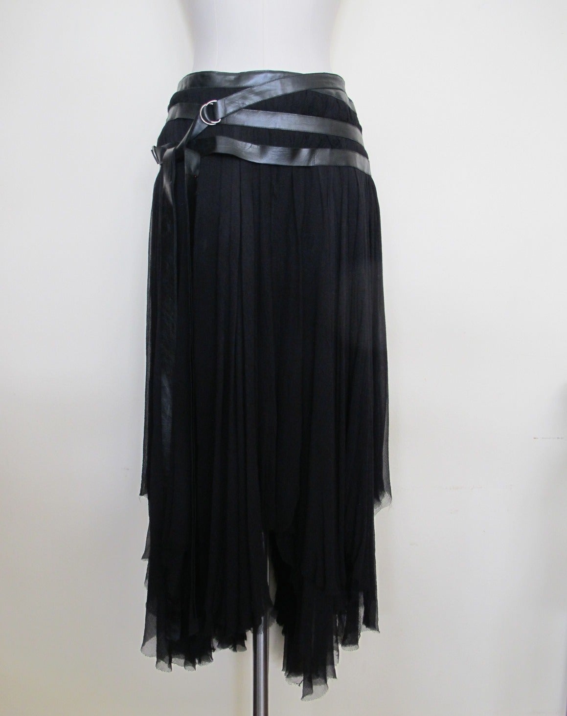 Hipster-Harness design black skirt with one inch genuine leather straps circling the hip with leather ties cascading to bottom of skirt. The silk chiffon has been created to cause the effect of different lengths. The wrap belt accentuates the beauty