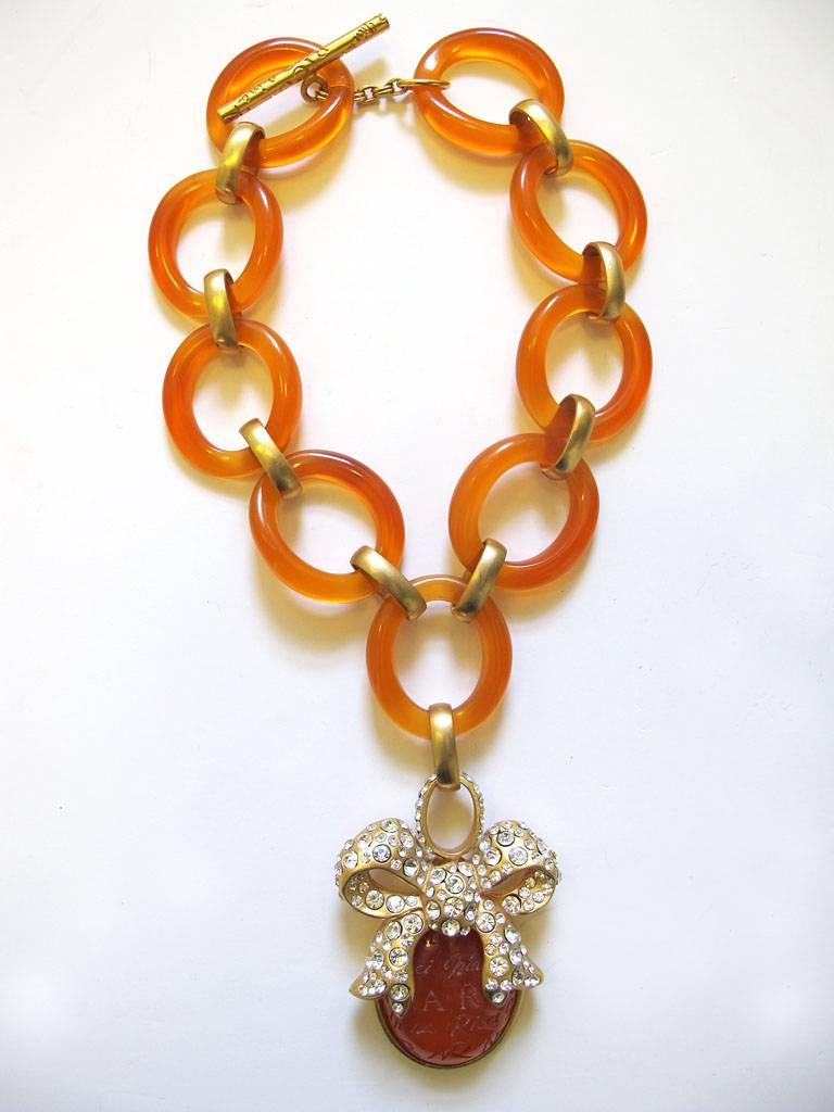 This vintage 1980's Nina Ricci oversized chain-link choker necklace is in a gold-tone and amber hued lucite. The pendant has a rhinestone incrusted bow and the lucite has 