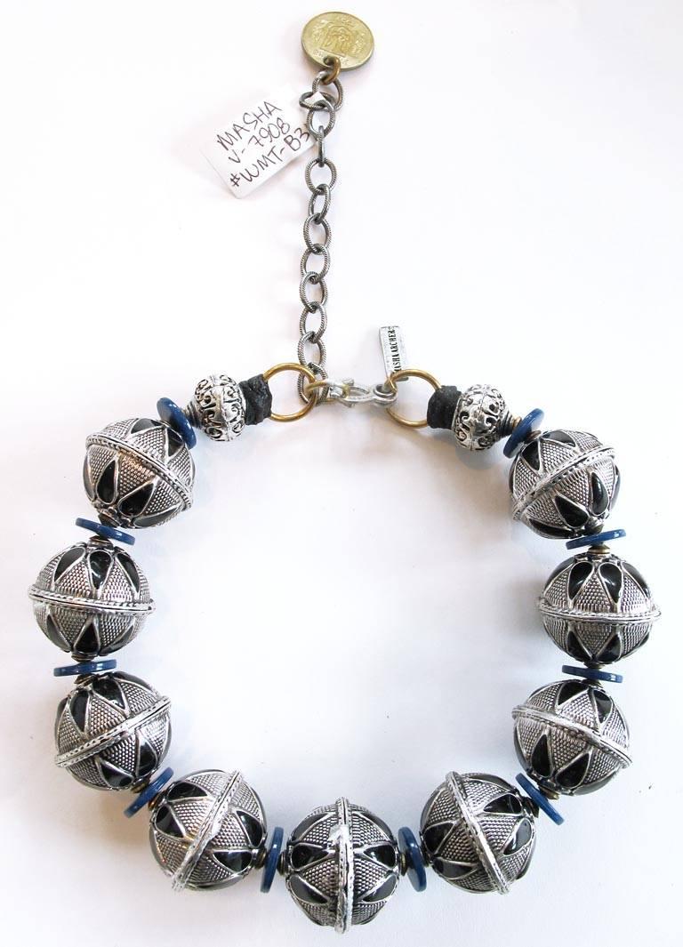 New Masha Archer single strand necklace of nine white brass stamped rounds with granulation style geometric motifs and black enameled drop cells (from China). Mounted with deep blue acrylic discs (from Japan). Finished with lead-free pewter
