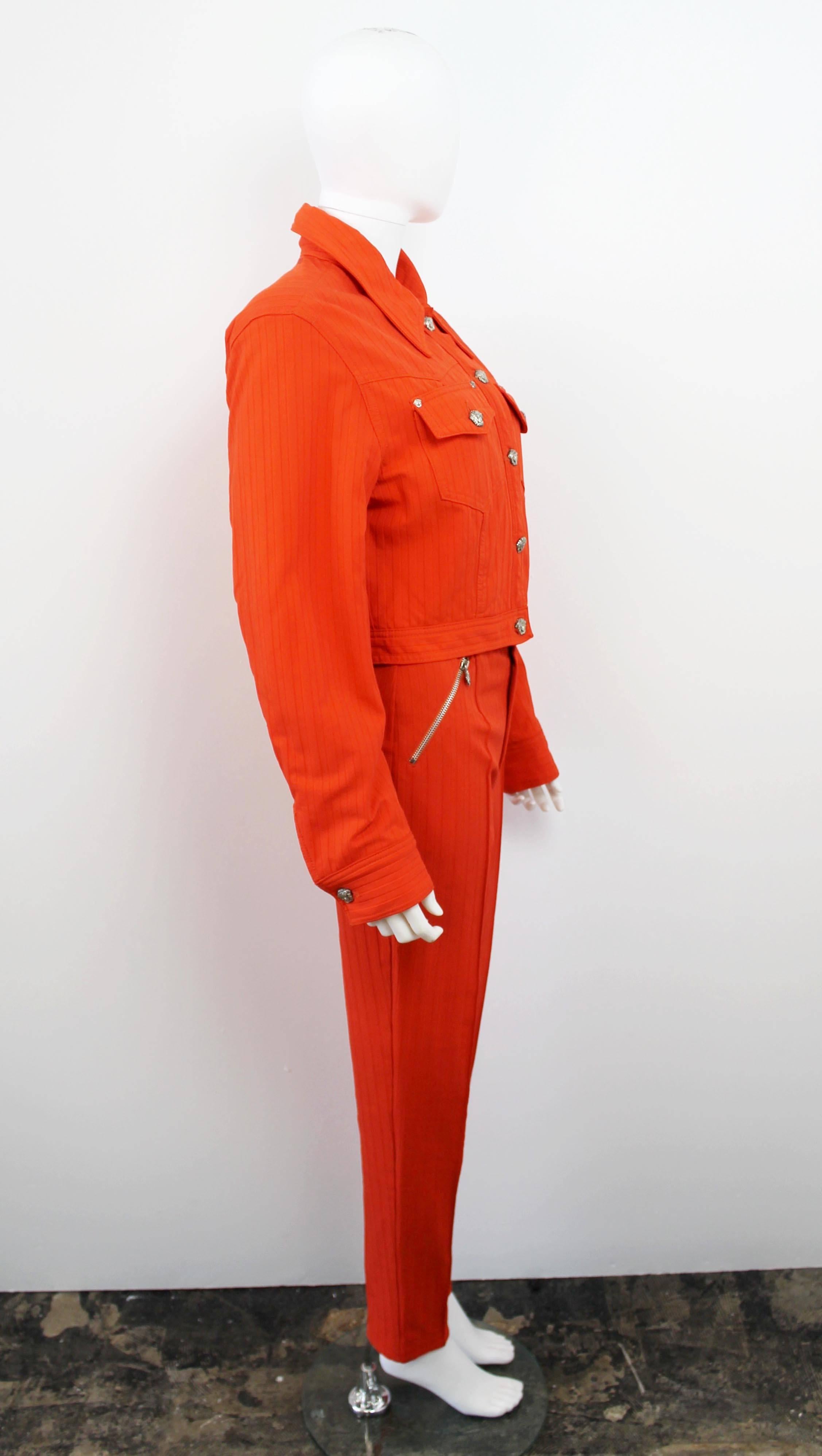 Vintage Versace Jeans Couture orange two-piece suit from the 1990's. Features silver Medusa head buttons and front zip pockets on the trousers. Has a stretchy high-waisted fit.