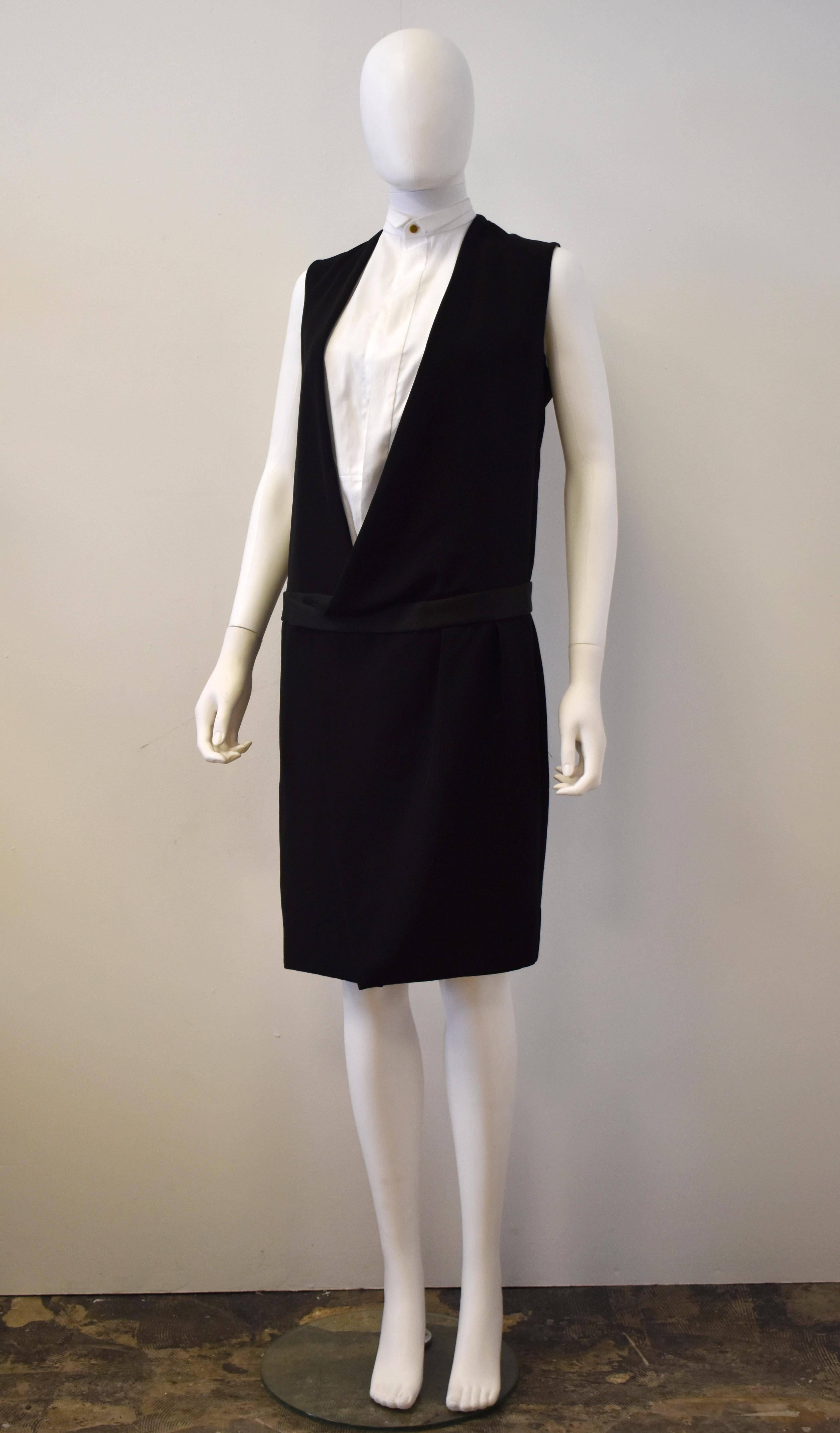 A beautiful and unworn black sleeveless tuxedo long coat with silk waistband and attached white sleeveless shirt inside. There is a single button and hook fastening at the hip, and darts along the front to create shape. Brand new without tags. The