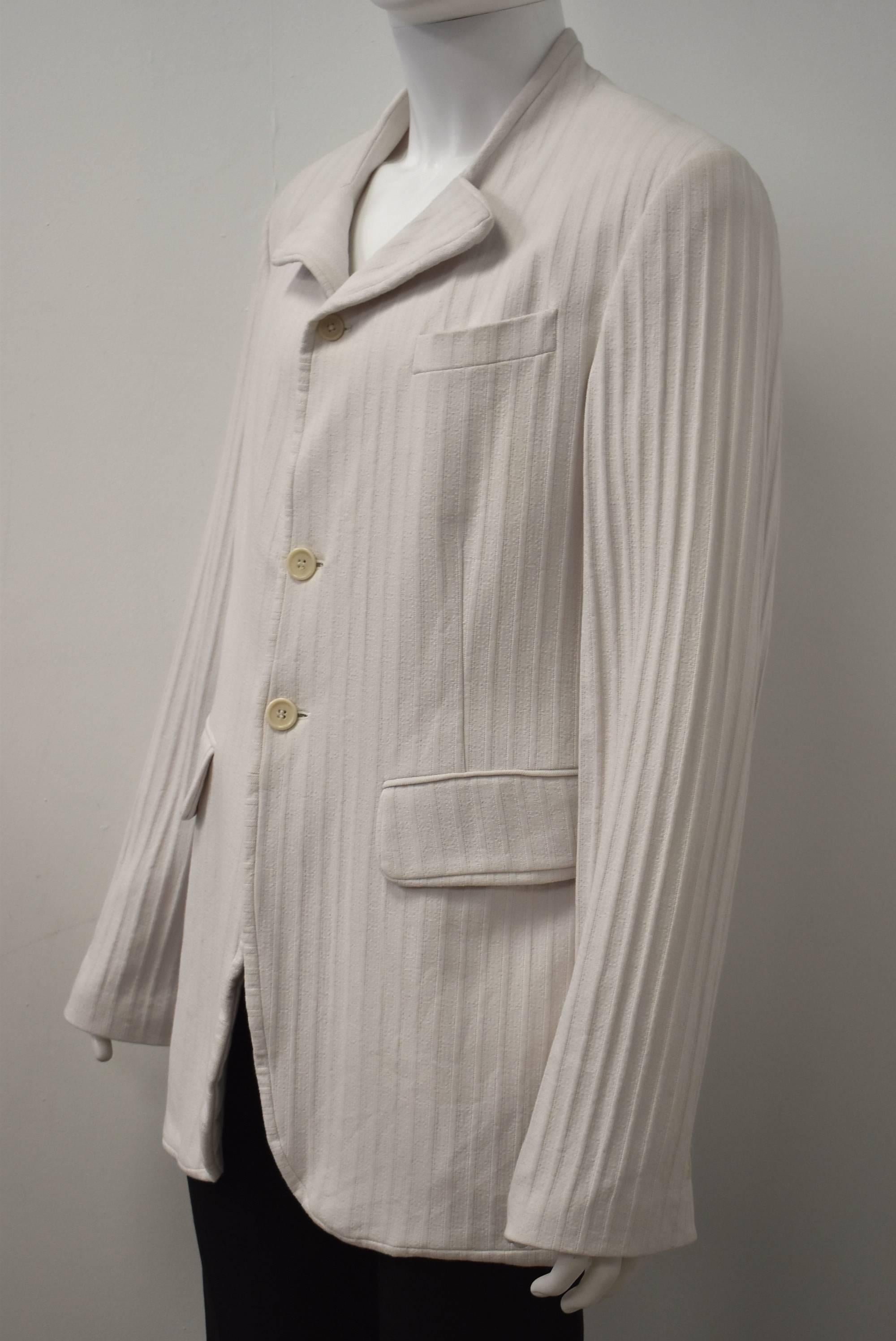 An interesting white jacket by Ann Demeulemeester. The jacket is made from a thick Striped/Ribbed cotton fabric. The jacket has a regular straight cut with pockets at the hip and button fastening. There is an unusual collar detail where it is