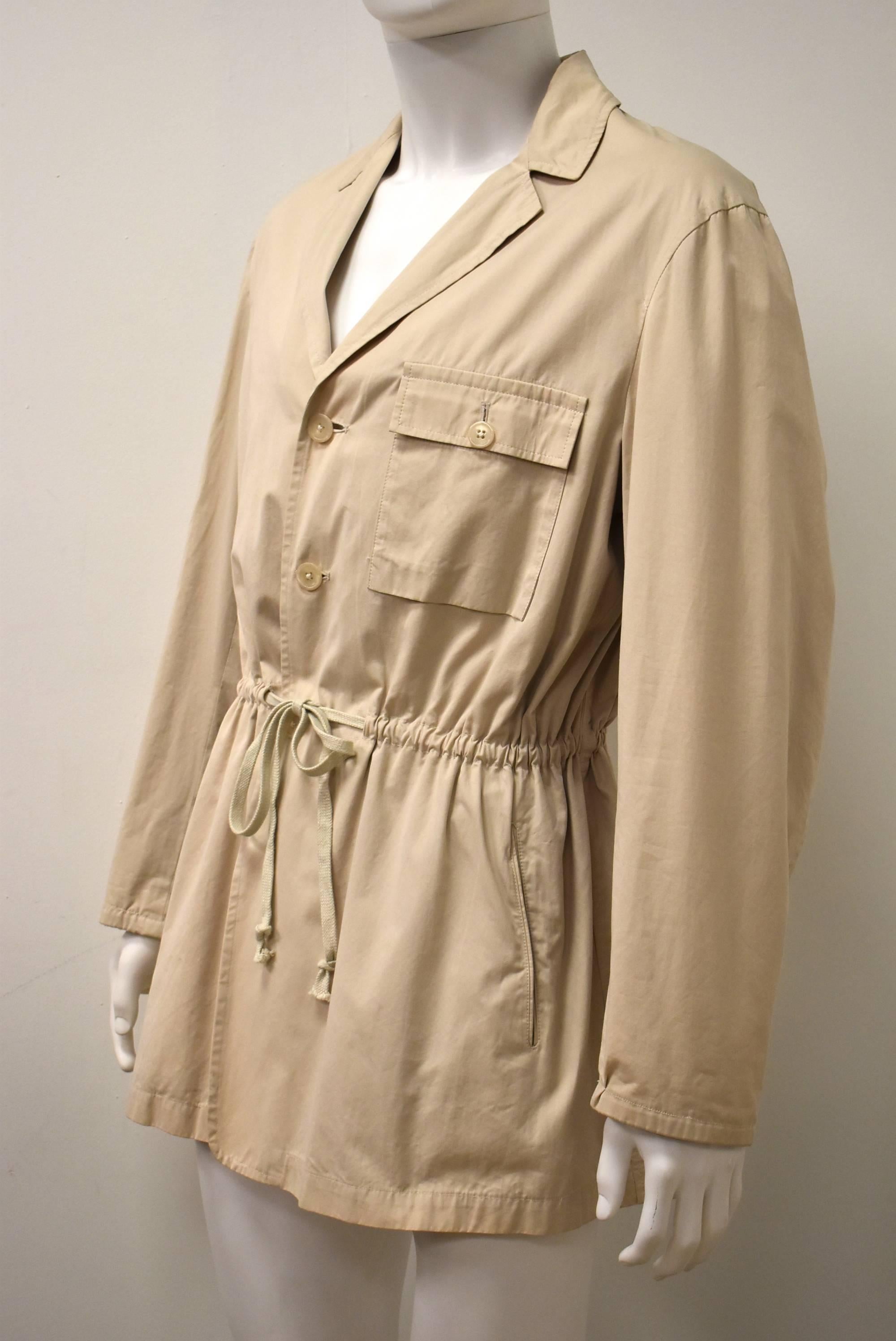 A cream coloured ’Safari’ style jacket by Japanese designer Yohji Yamamoto dating from the 1980’s. The jacket has a simple shape with a drawstring at the waist to create a fitted silhouette. It has a button-down front, two pockets at the hip and a