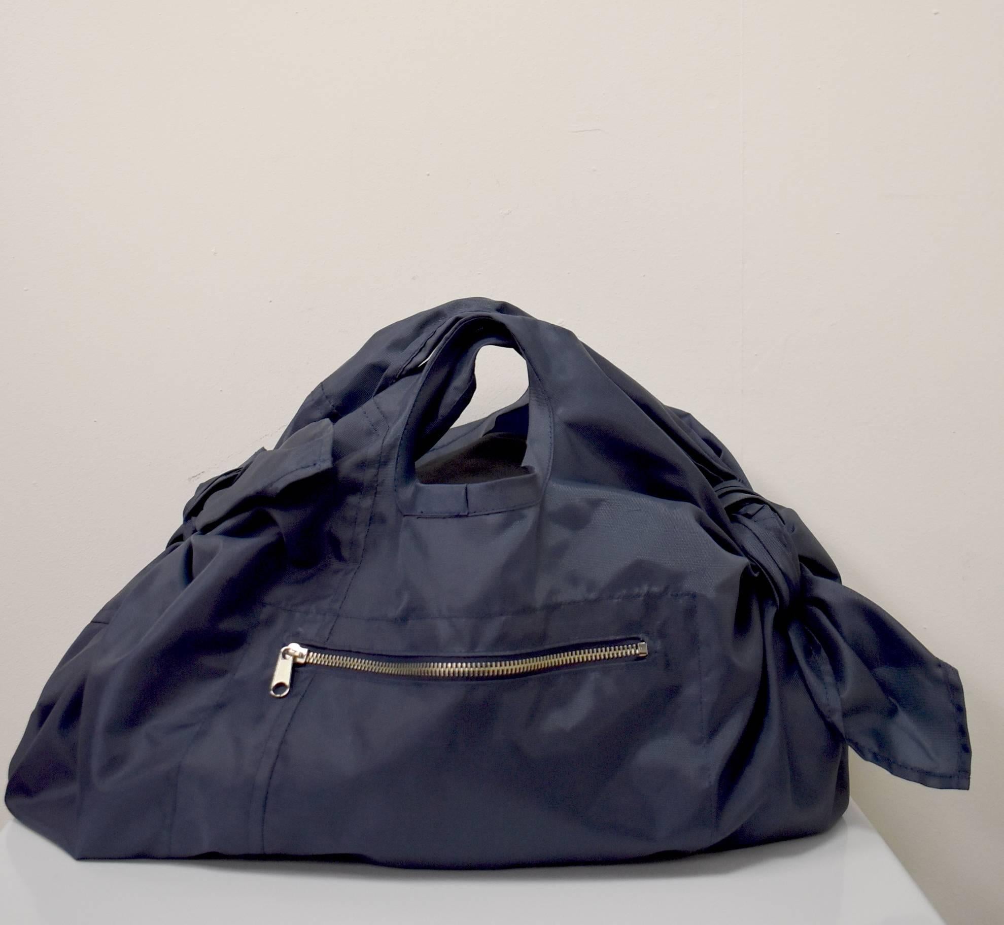 This Comme des Garcons Navy handbag has a soft rectangular shape with two short shoulder straps which can be knotted and tied to create a longer or shorter length. The bag is made from a sporty synthetic material and has a zip pocket on the front.