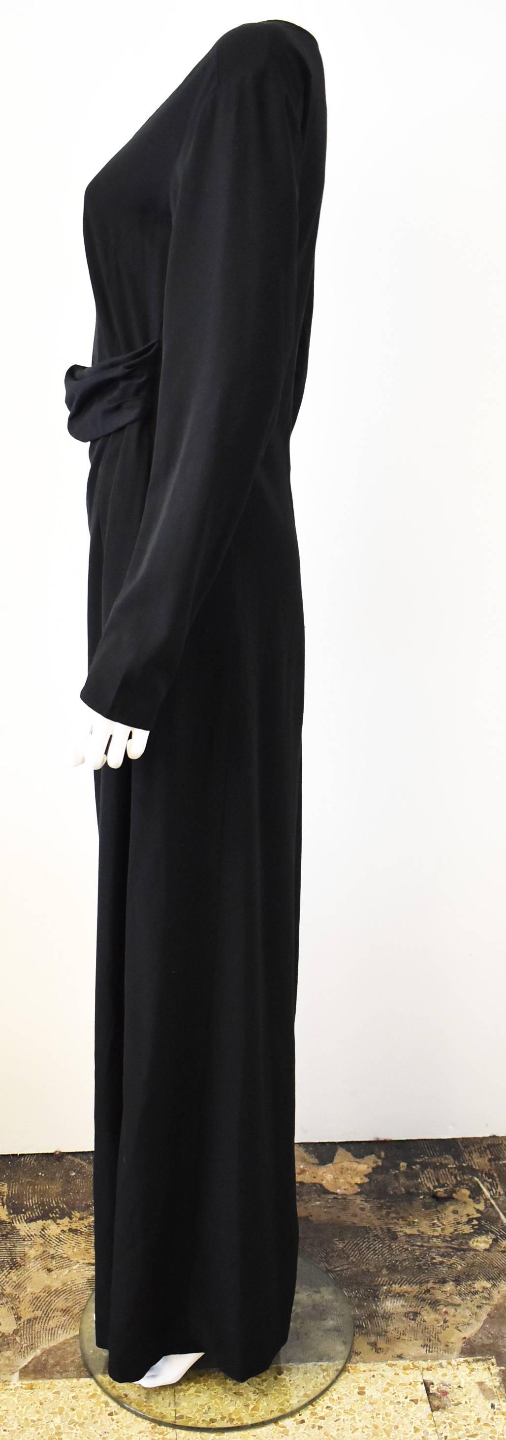 A floor-length black dress with long sleeves by Belgian designer Dries Van Noten. The dress has a simple A-line shape, round collar, and loose shape but has an unusual opening at the front along the waistline. This gap creates a sort of ‘tucked in