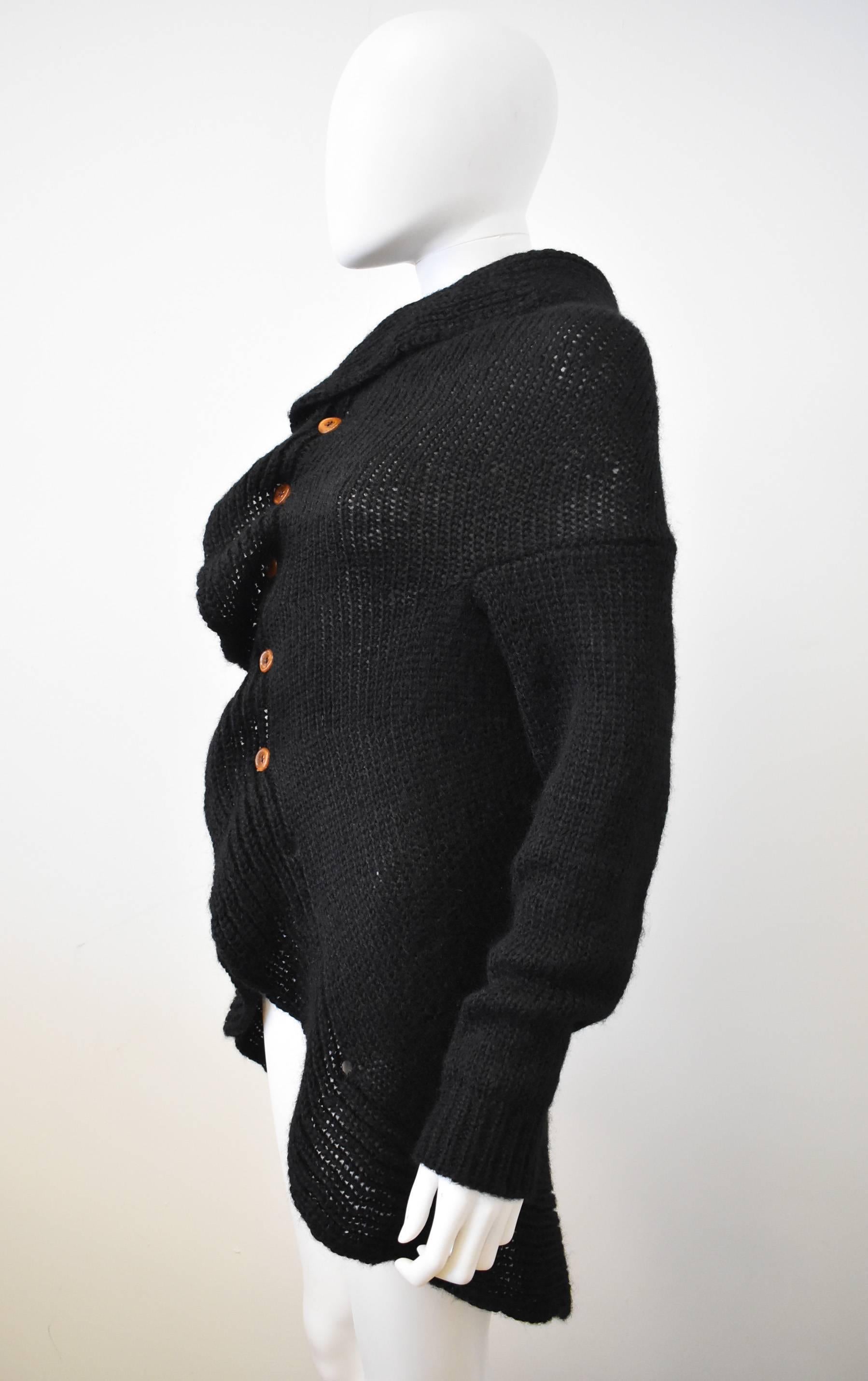 This black 2002 cardigan by Comme des Garcons has a wonderful shape with a high collar, central button fastening and a scoop line hem. The front has a frill that flows along the opening and  is made from a Mohair and Acrylic blend. It is a chunky