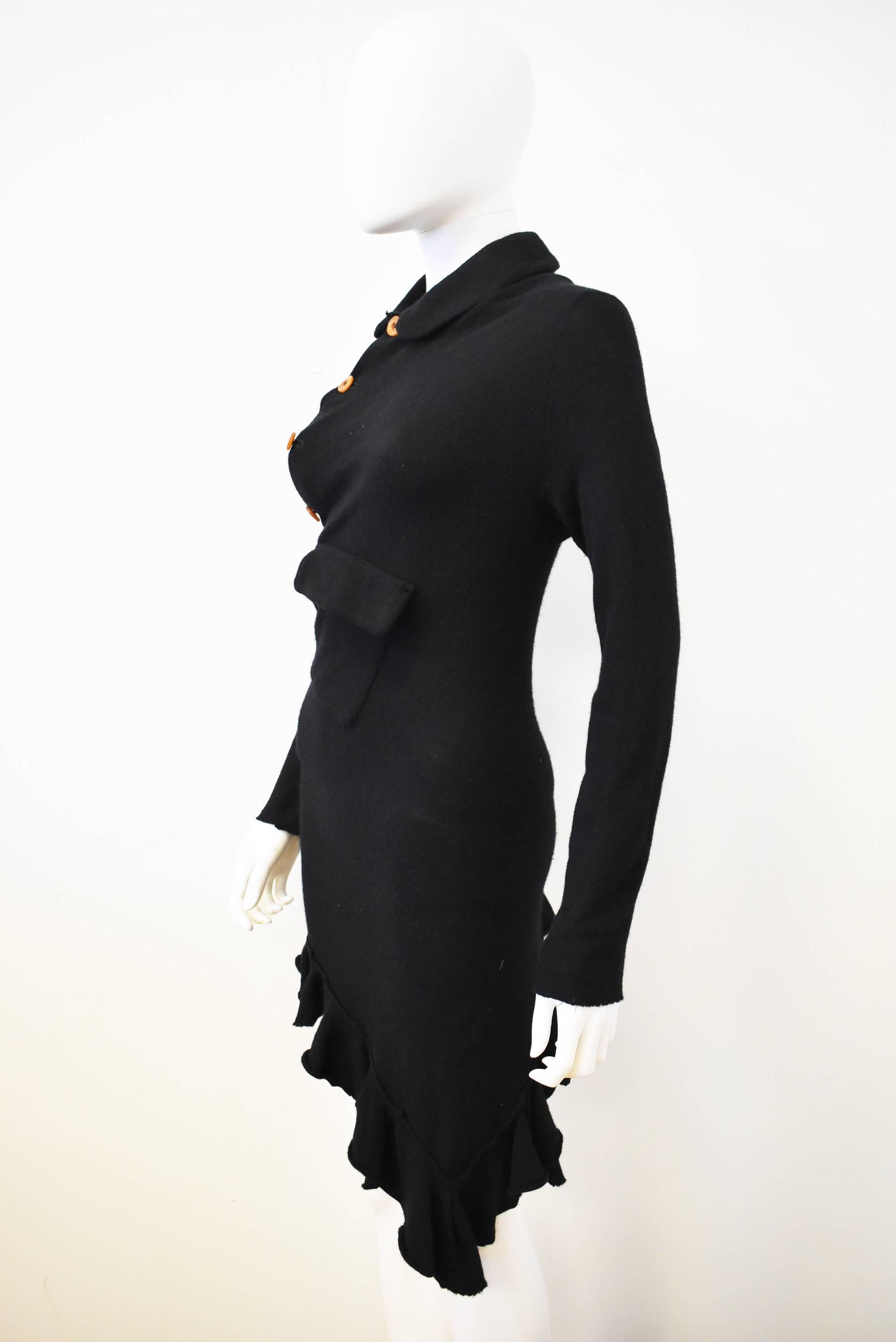 This black Comme des Garcons knitted dress from 2002 has an unusual shape with an asymmetric hem, and twisted style that flows around the body. The button up front goes across the body diagonally and created folds across the front and back. There