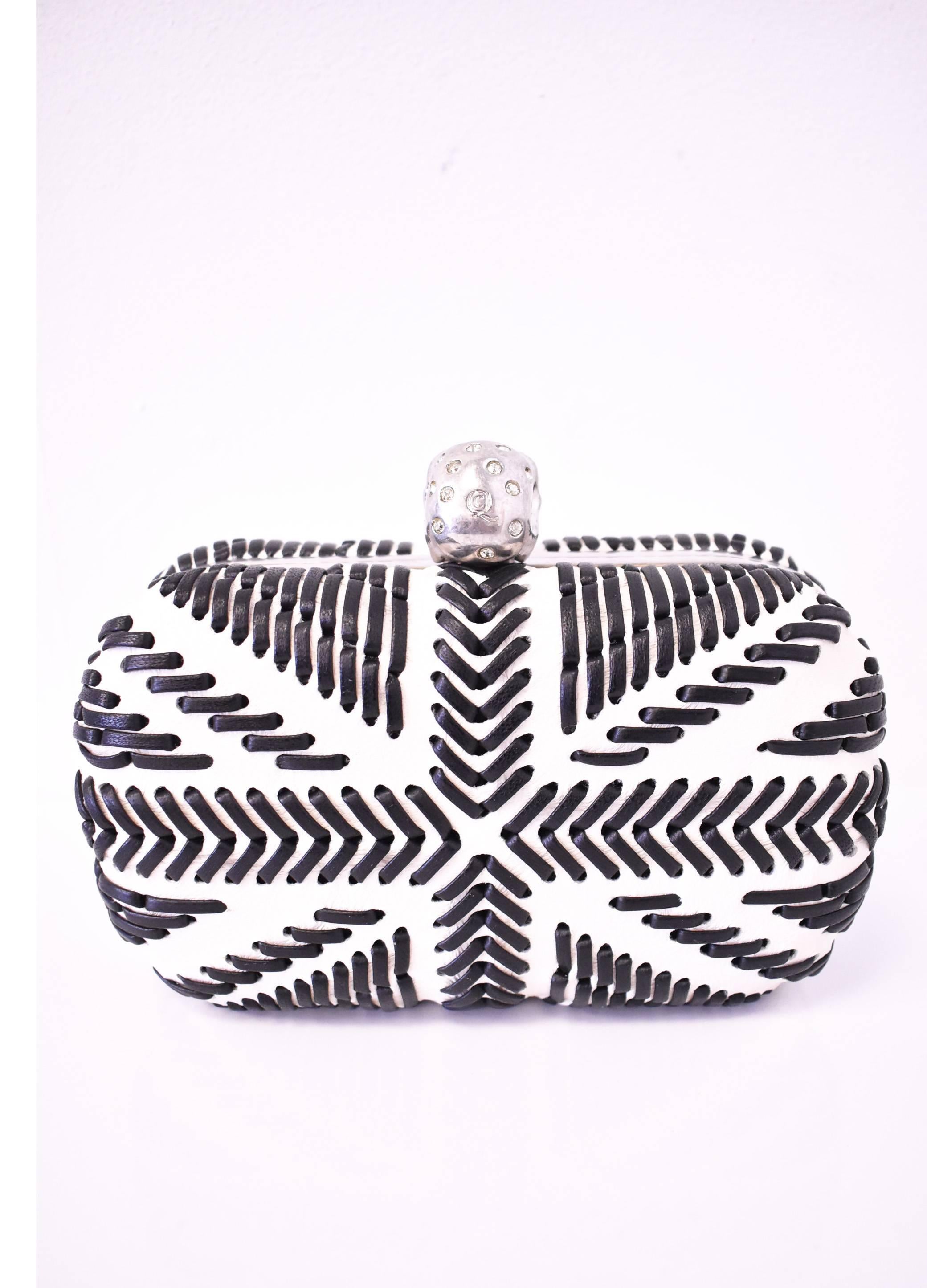 This signature Alexander McQueen box clutch/purse is made of white leather with a black leather whipstitched Union Jack pattern. It features the iconic embellished skull clasp set with pearlescent eyes and crystals. The hard-shell clutch has rounded